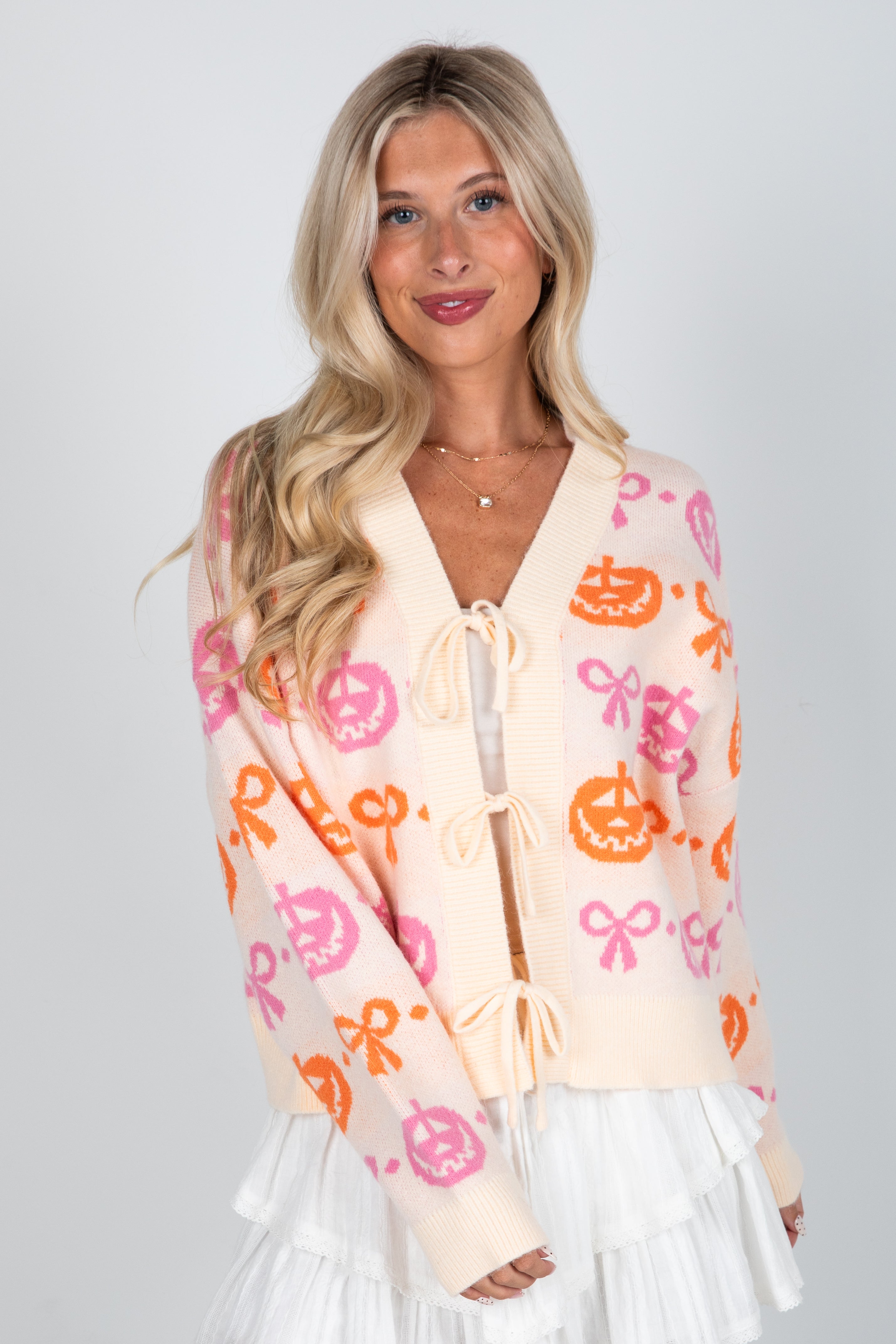 Woman wearing a patterned cardigan with pumpkins and flowers on a plain background