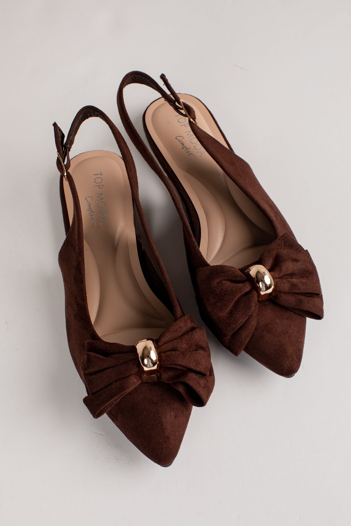 A pair of dark brown suede slingback pointed-toe flats with a large bow on the toe and a small gold-tone metal accent, displayed on a light gray background.