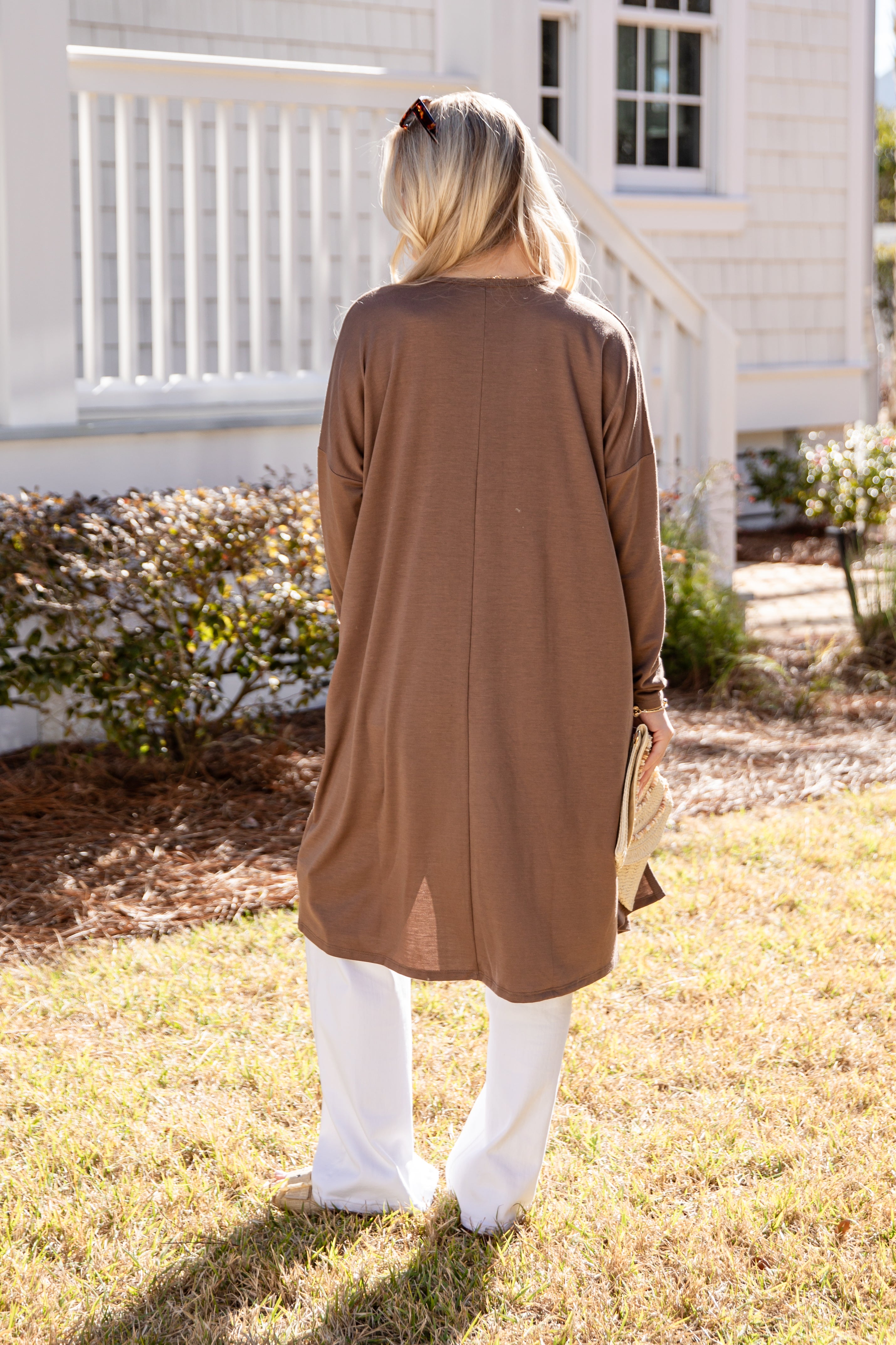Person wearing a brown long-sleeve cardigan standing outdoors.