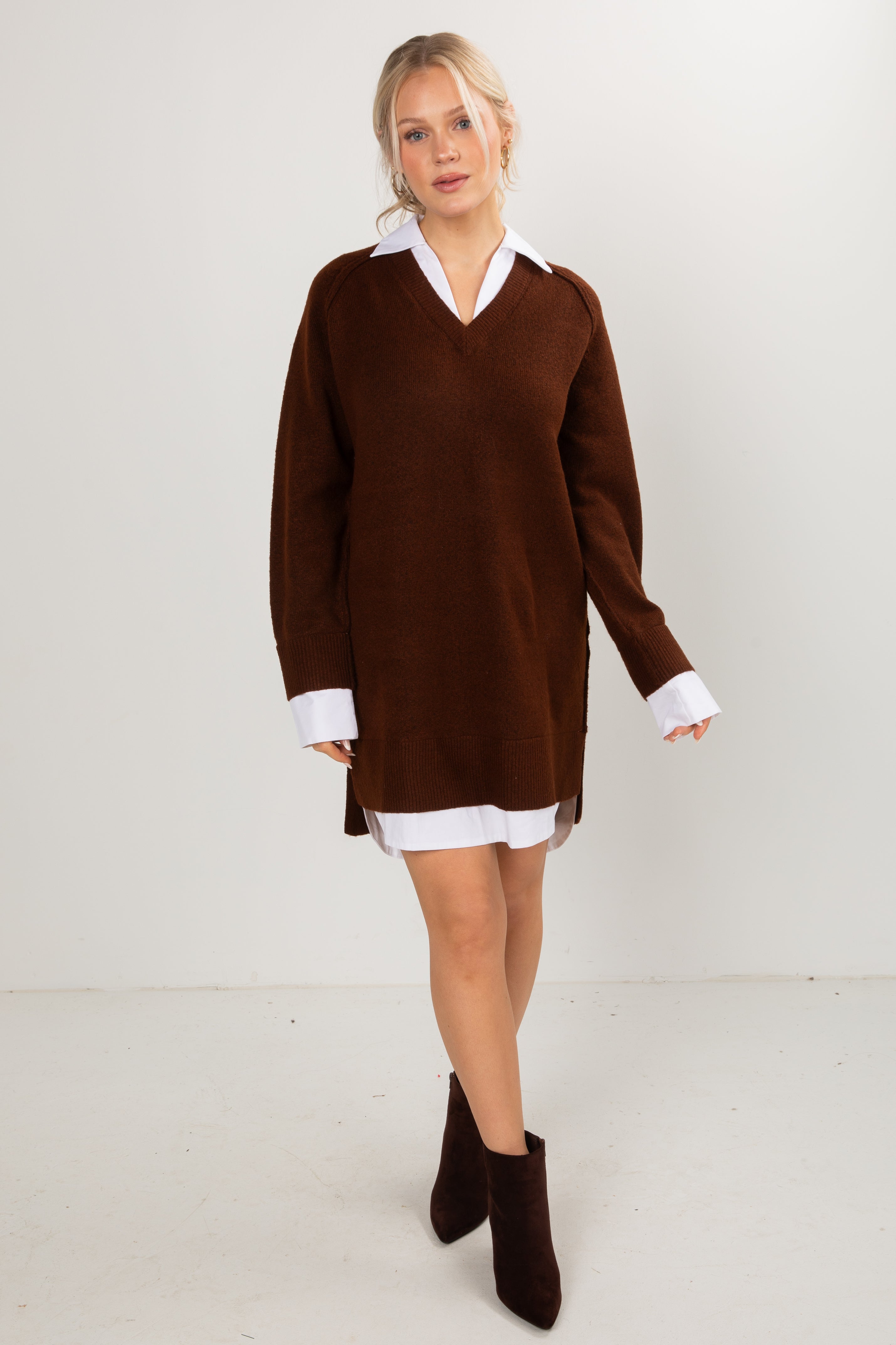 Woman wearing a brown V-neck sweater dress with a white collared shirt, styled with dark brown ankle boots.