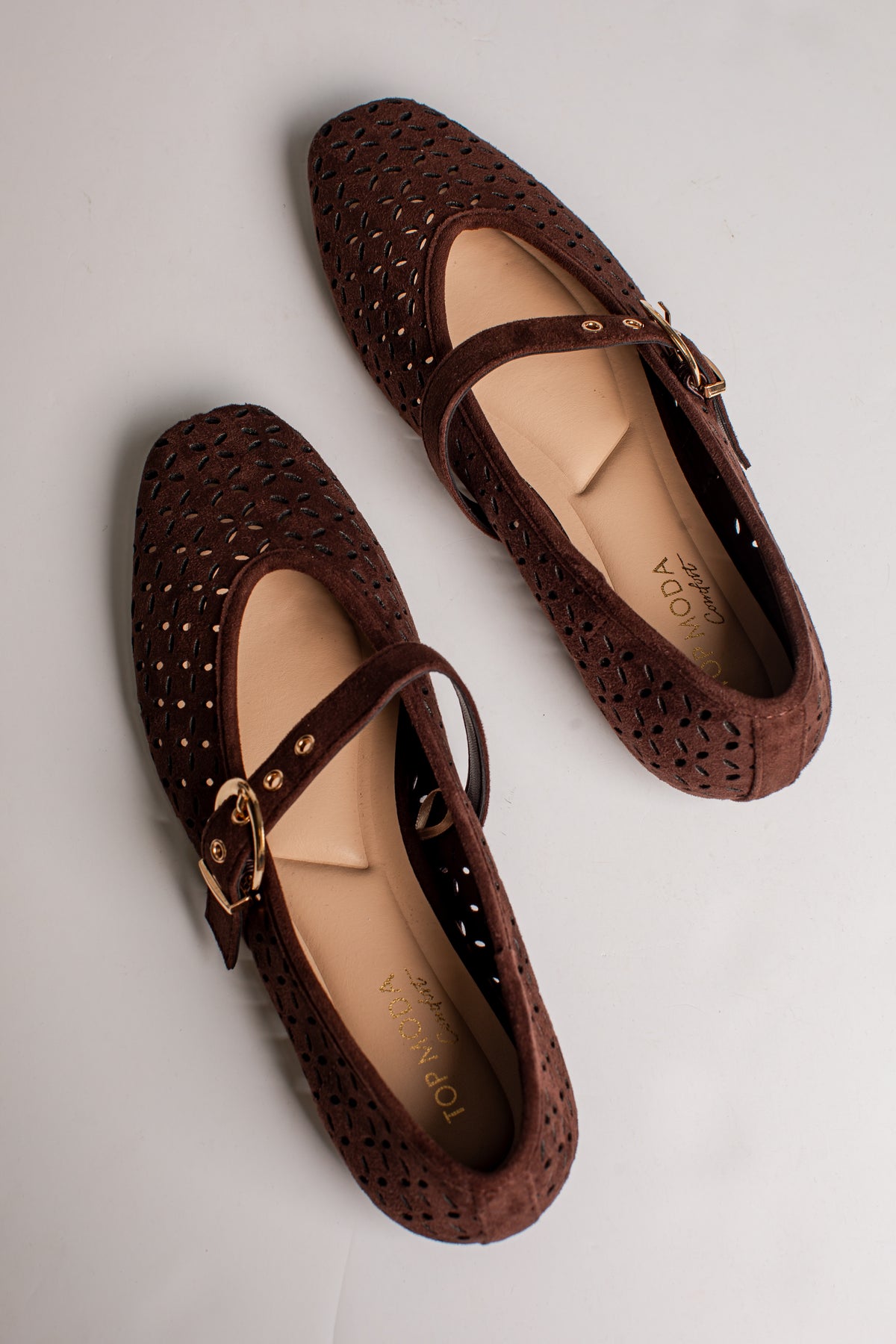 A pair of dark brown woven Mary Jane flats with gold-tone buckle straps, shown from a top-down angle on a light gray background.