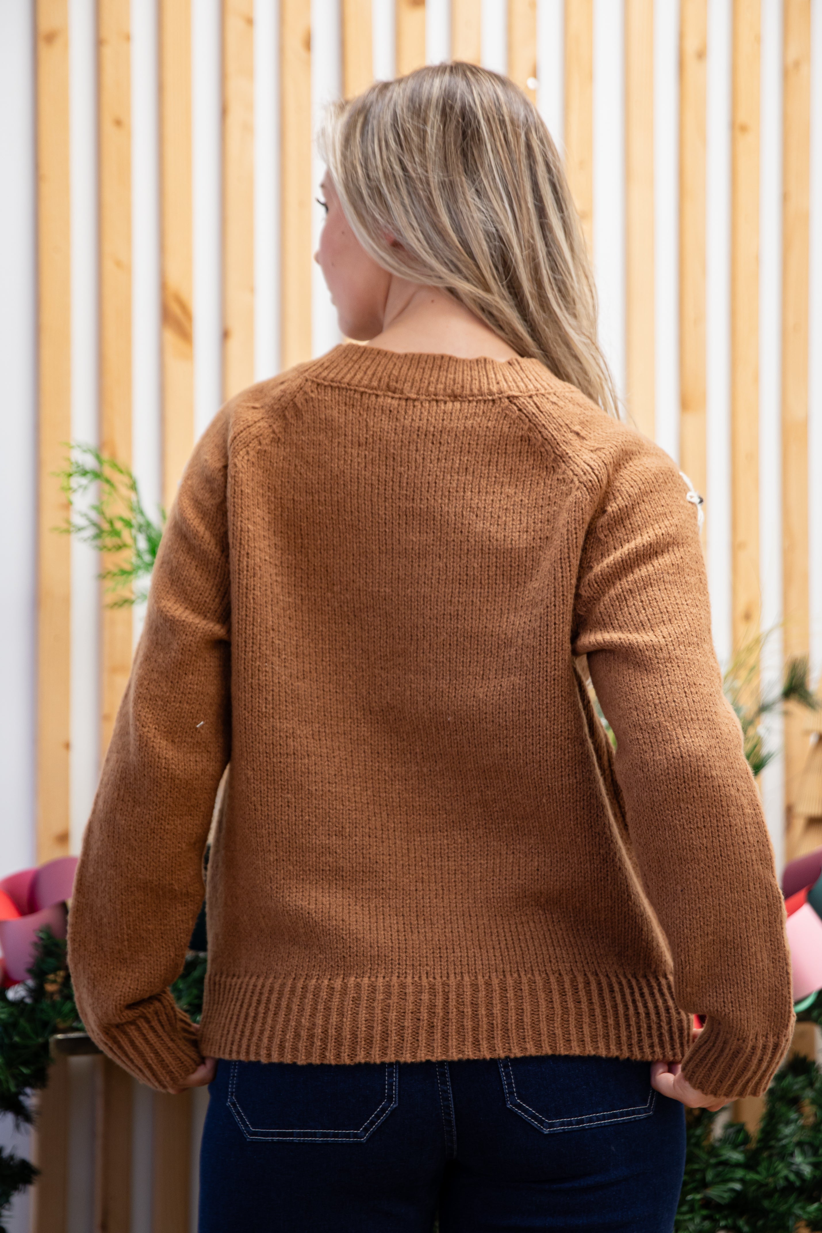 Person wearing a brown sweater standing in front of a wooden fence.
