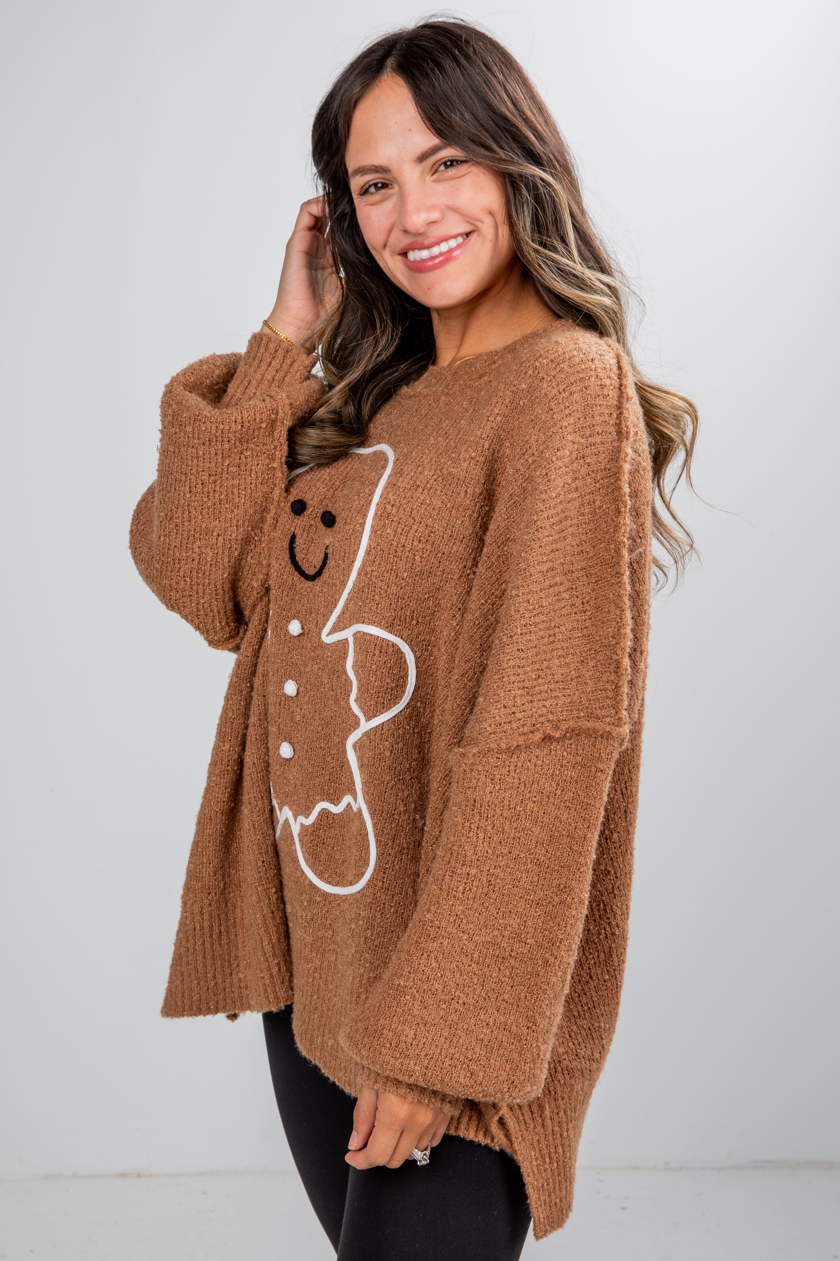 Woman wearing a brown sweater with a gingerbread man design on a white background