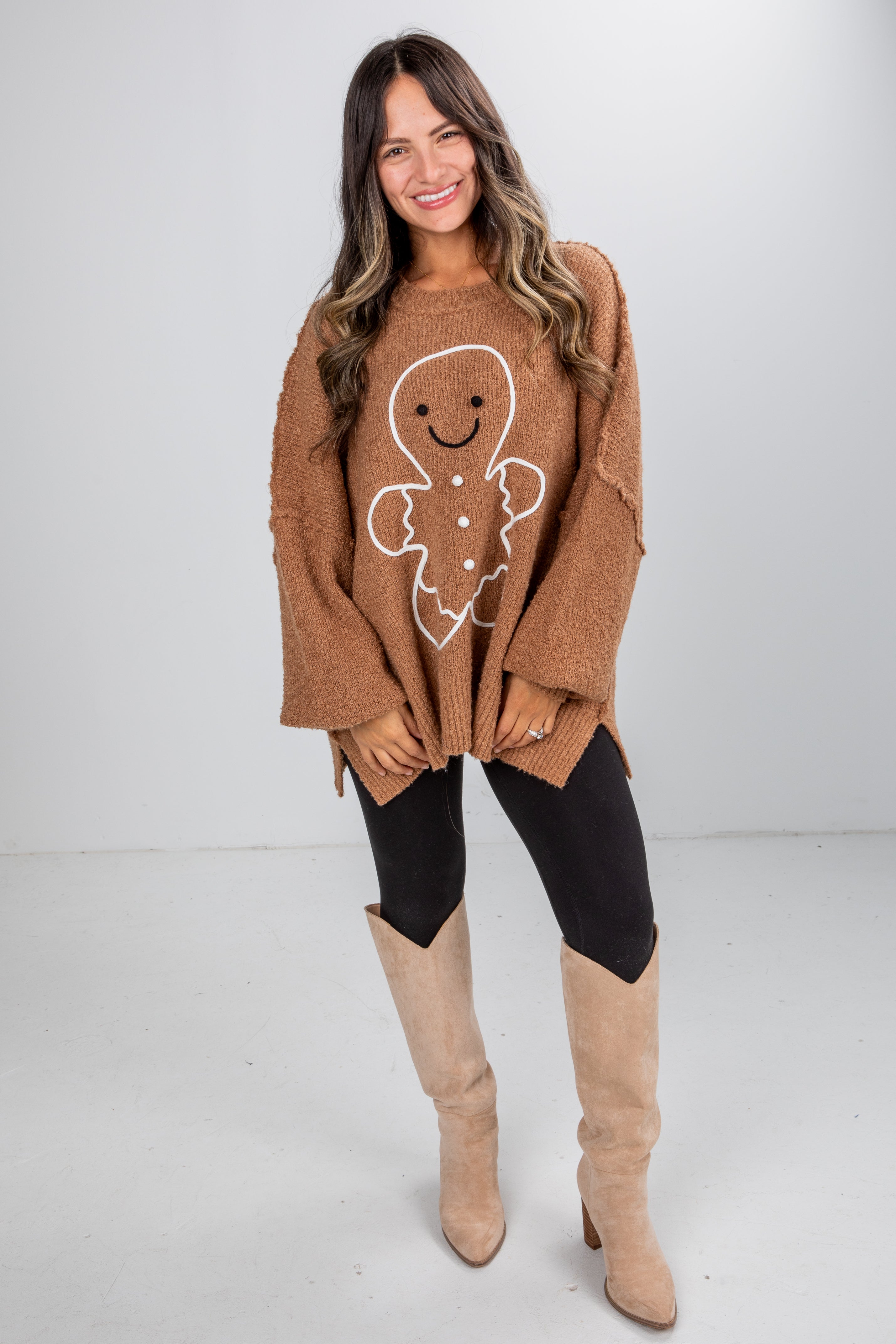 Woman wearing a brown sweater with a gingerbread man design and beige knee-high boots on a white background