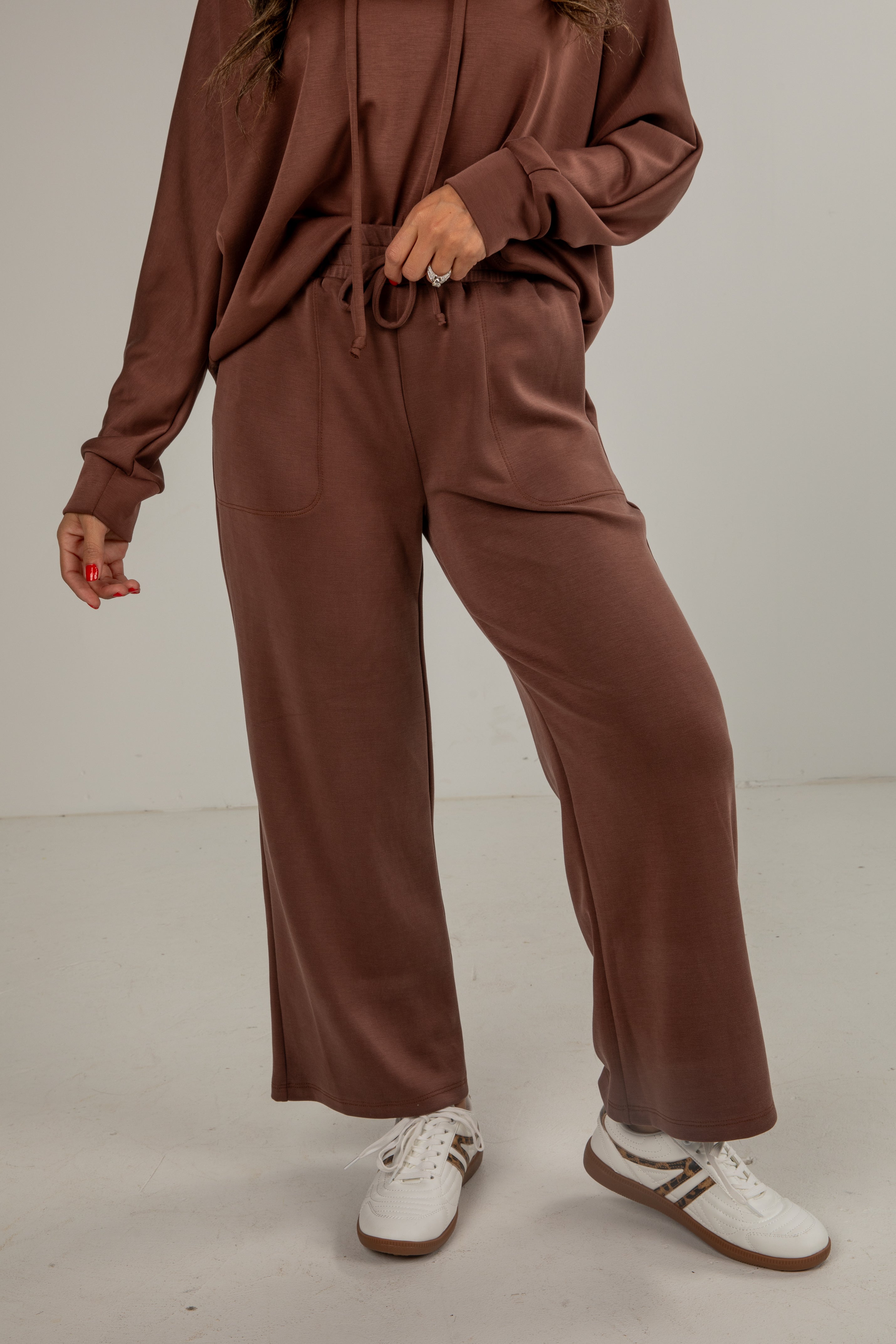 Person wearing a brown tracksuit with white sneakers on a plain background