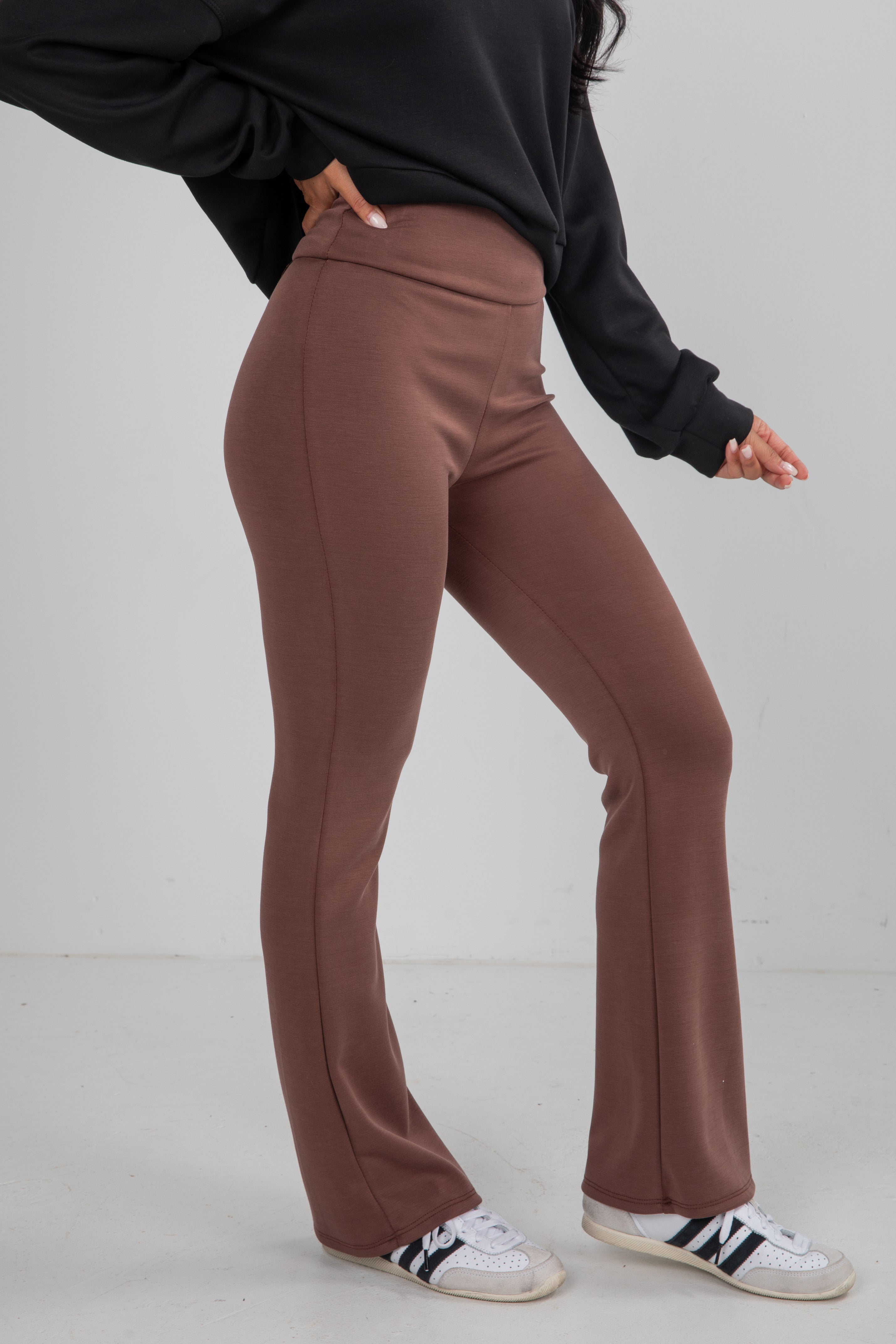 Person wearing brown pants and black Adidas shoes on a white background