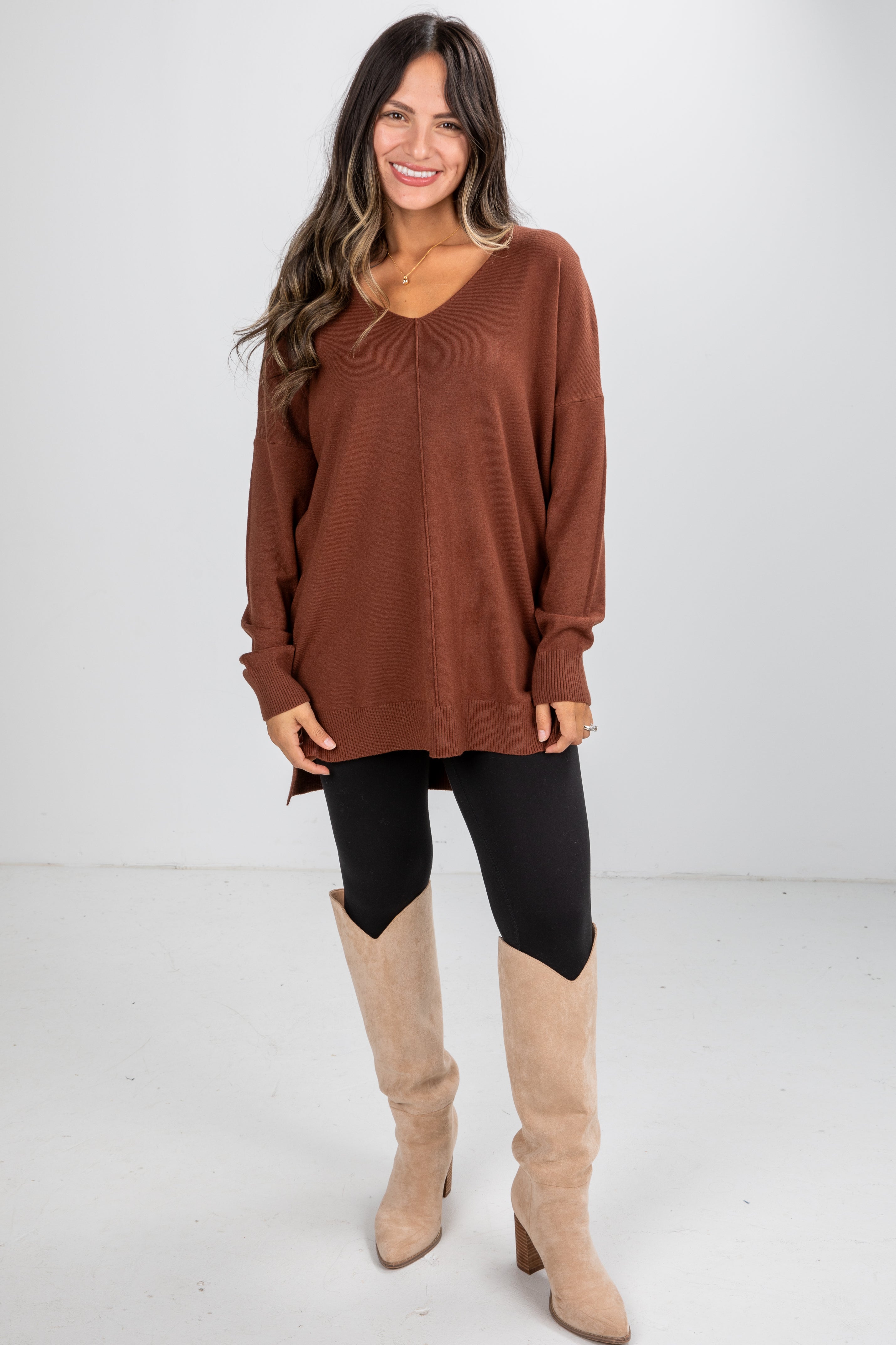 Woman wearing a brown sweater and black leggings with beige knee-high boots on a white background