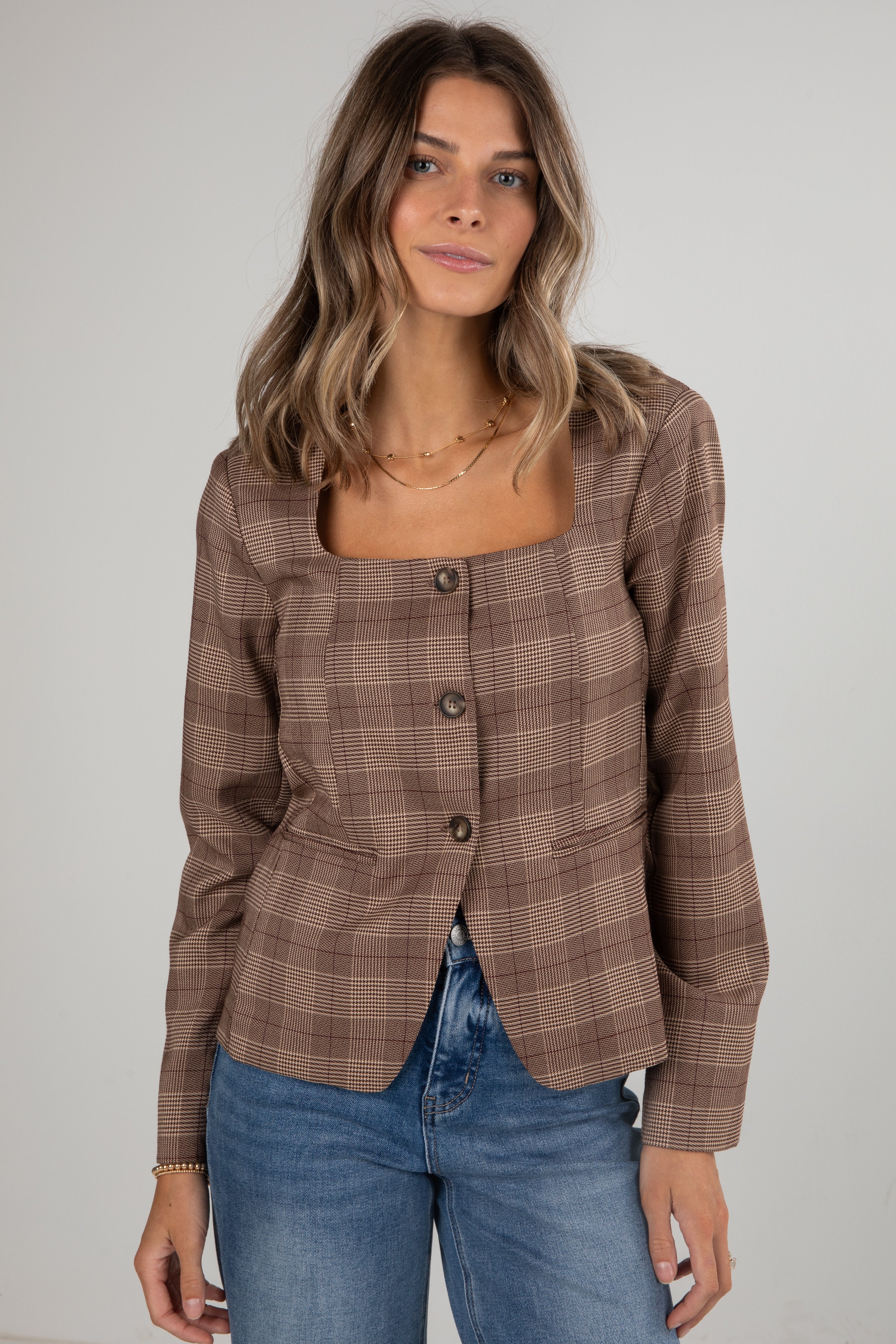 Woman wearing a brown plaid blazer and blue jeans against a plain background