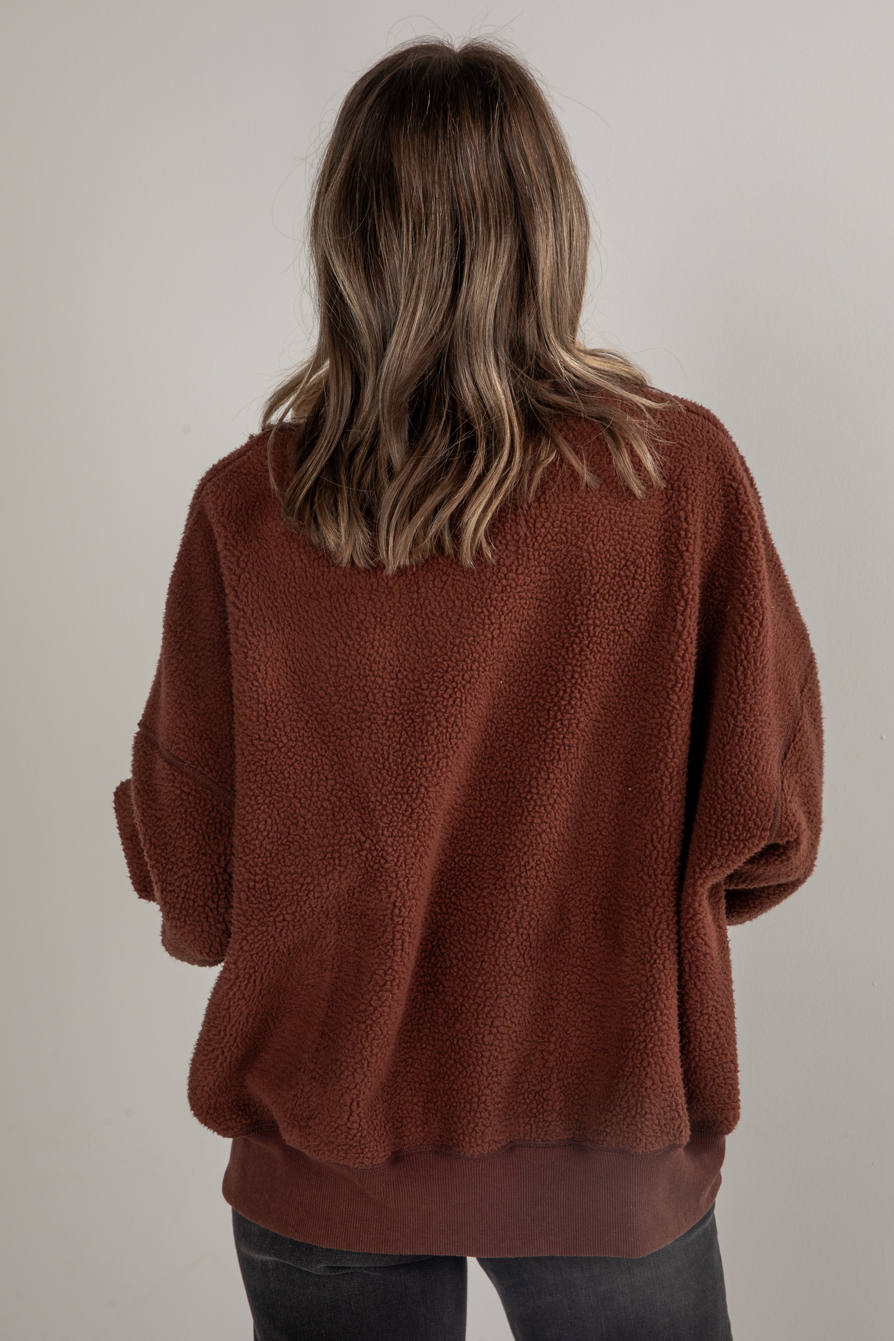 Person wearing a brown sweater from behind on a plain background
