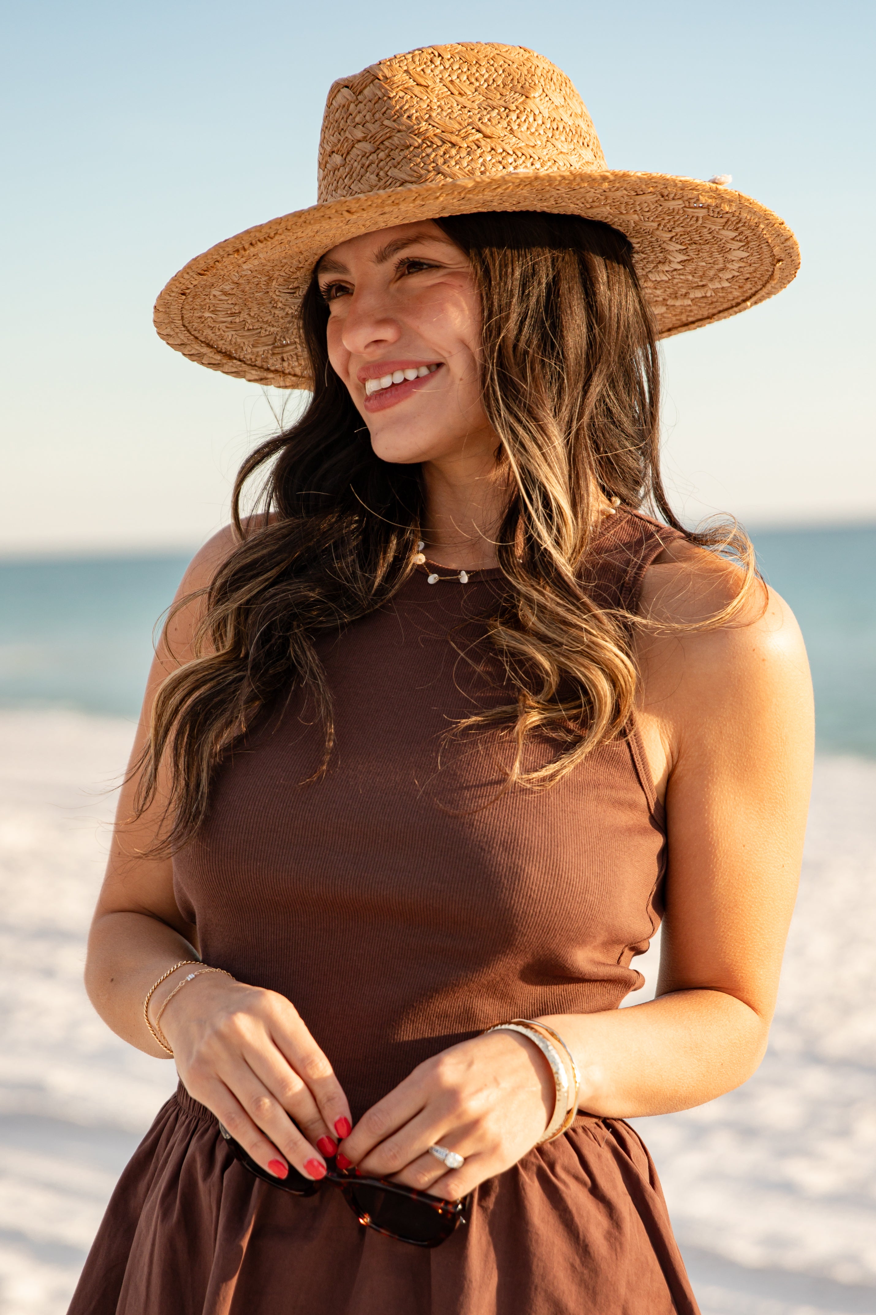 Woman wearing a brown dress and straw hat on a beach