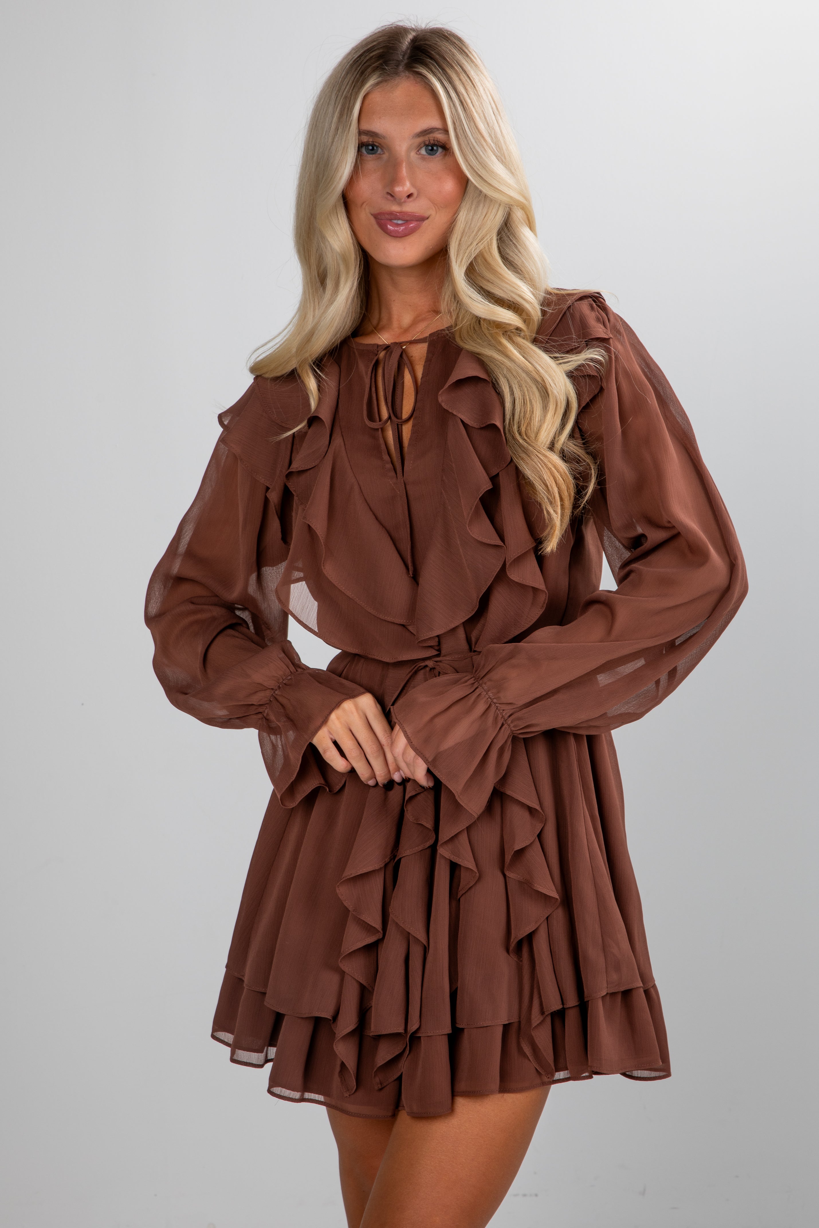 Woman wearing a brown ruffled dress against a plain background