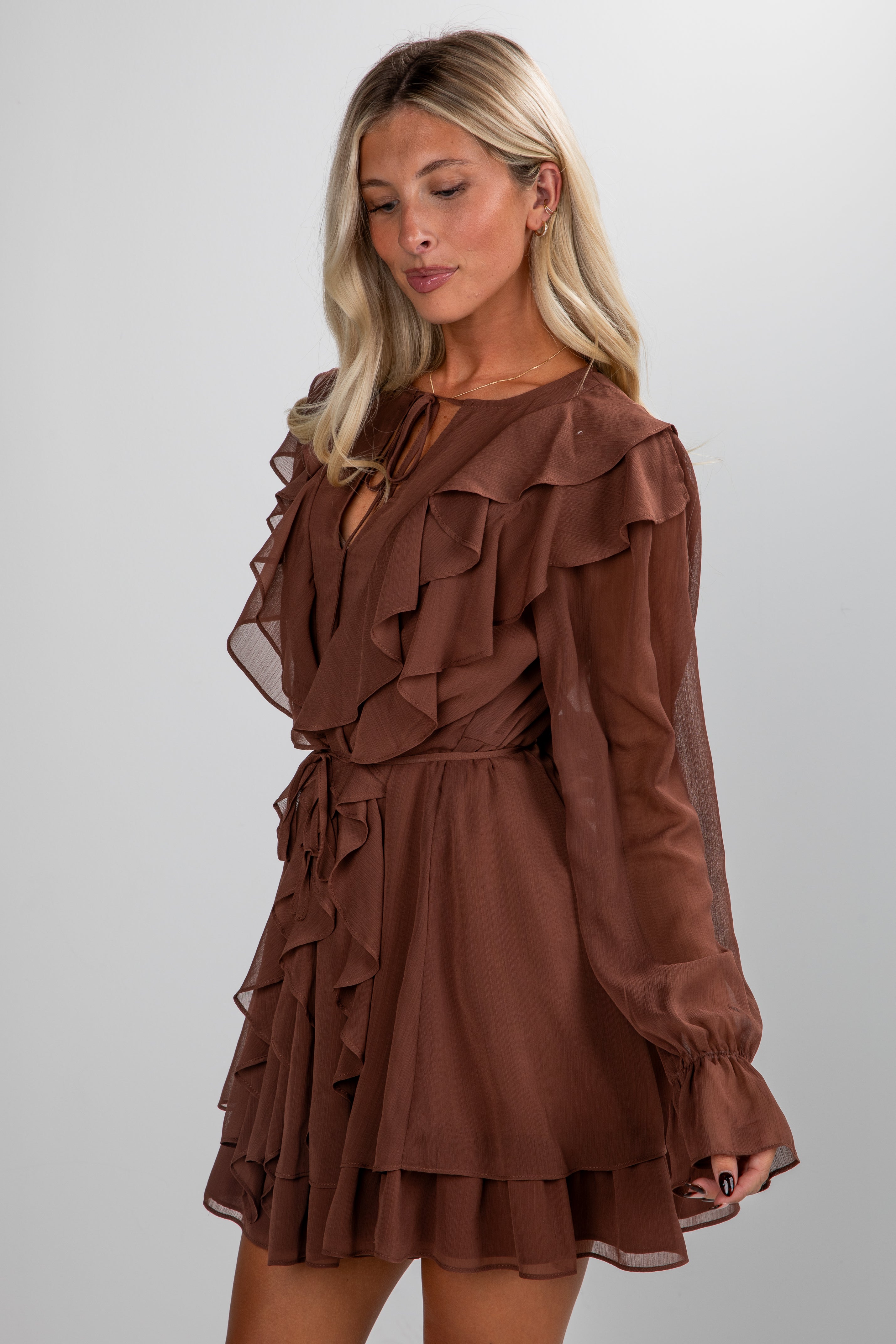 Woman wearing a brown ruffled dress against a plain background