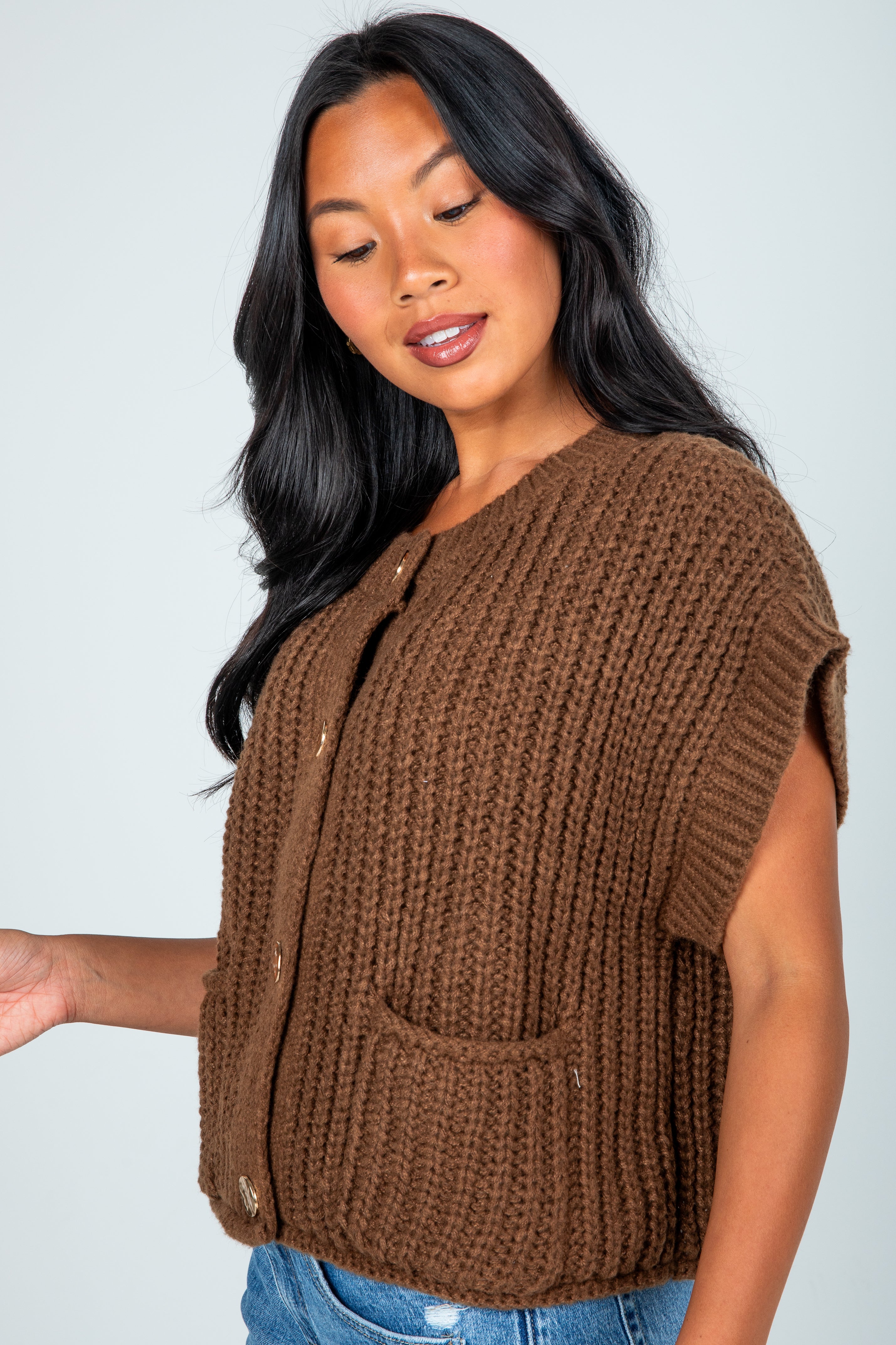 Woman wearing a brown knitted vest against a plain background