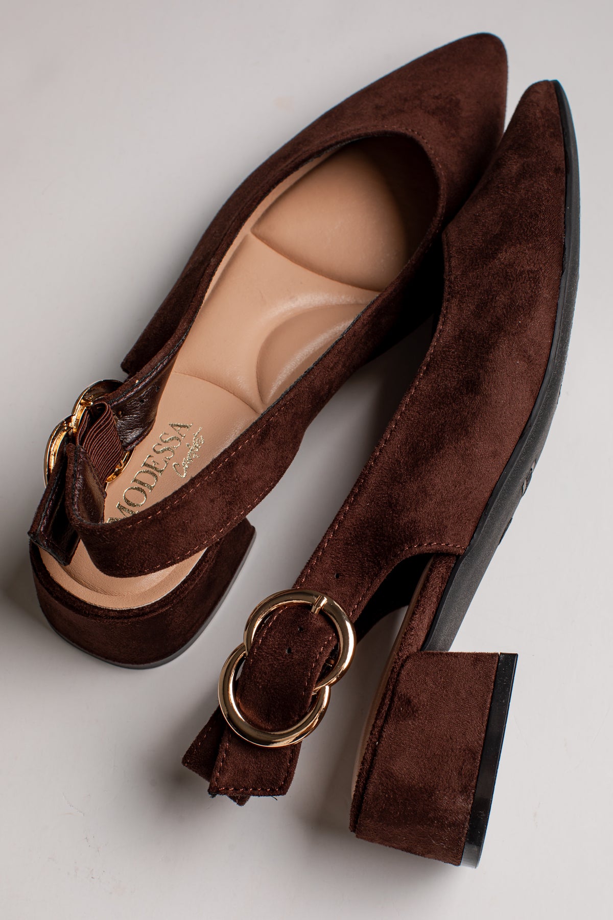 A pair of dark brown suede block-heel pumps with gold-tone ring hardware and ankle straps, displayed on a light gray background.