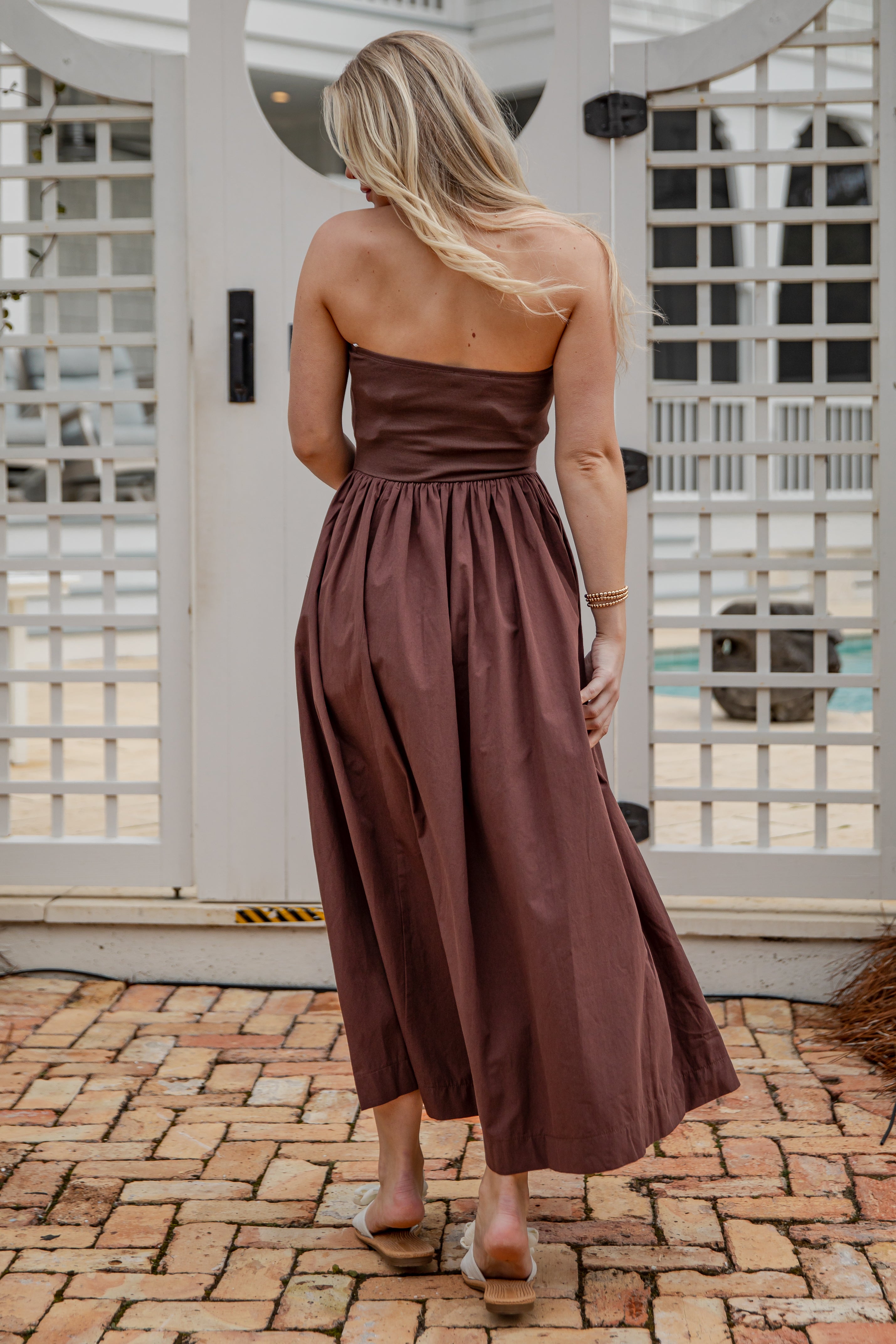 Woman wearing a brown strapless dress standing on a brick patio.