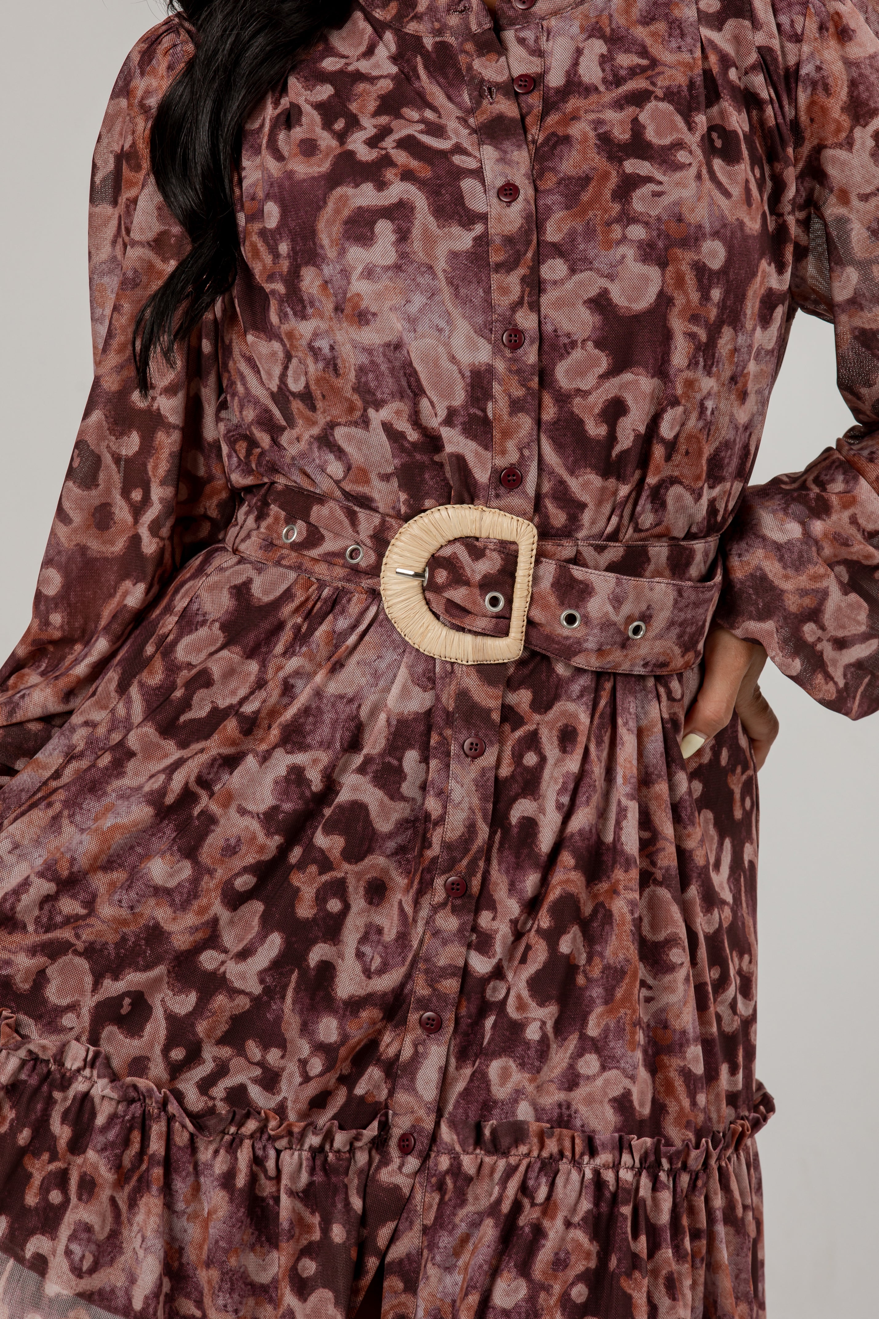 A close-up of a long-sleeve button-front dress with an abstract animal-like print in dusty mauve, brown, and burgundy tones, featuring a matching waist belt with a large round natural-fiber buckle.