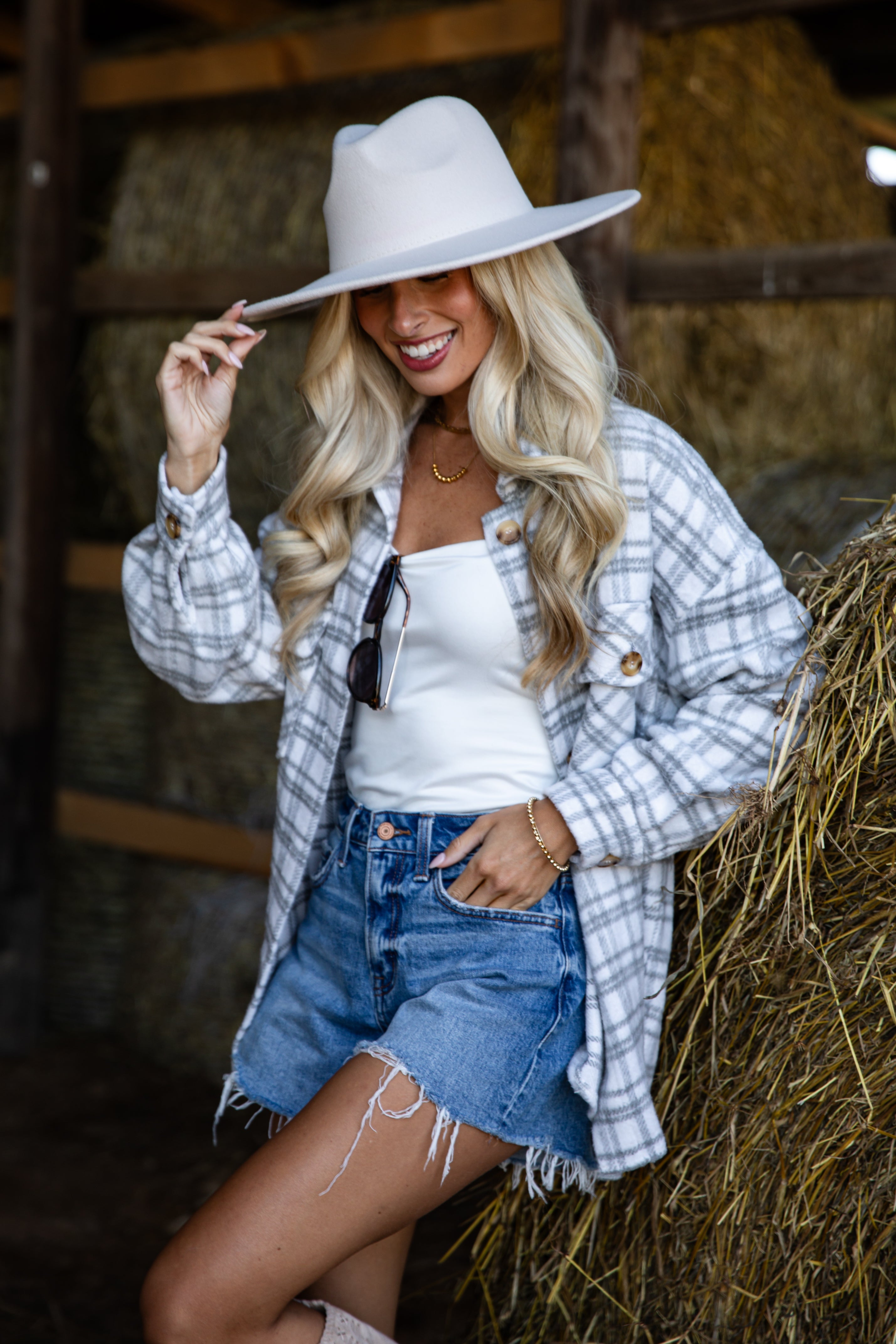 Woman wearing a white hat, plaid shirt, and denim skirt in a barn setting