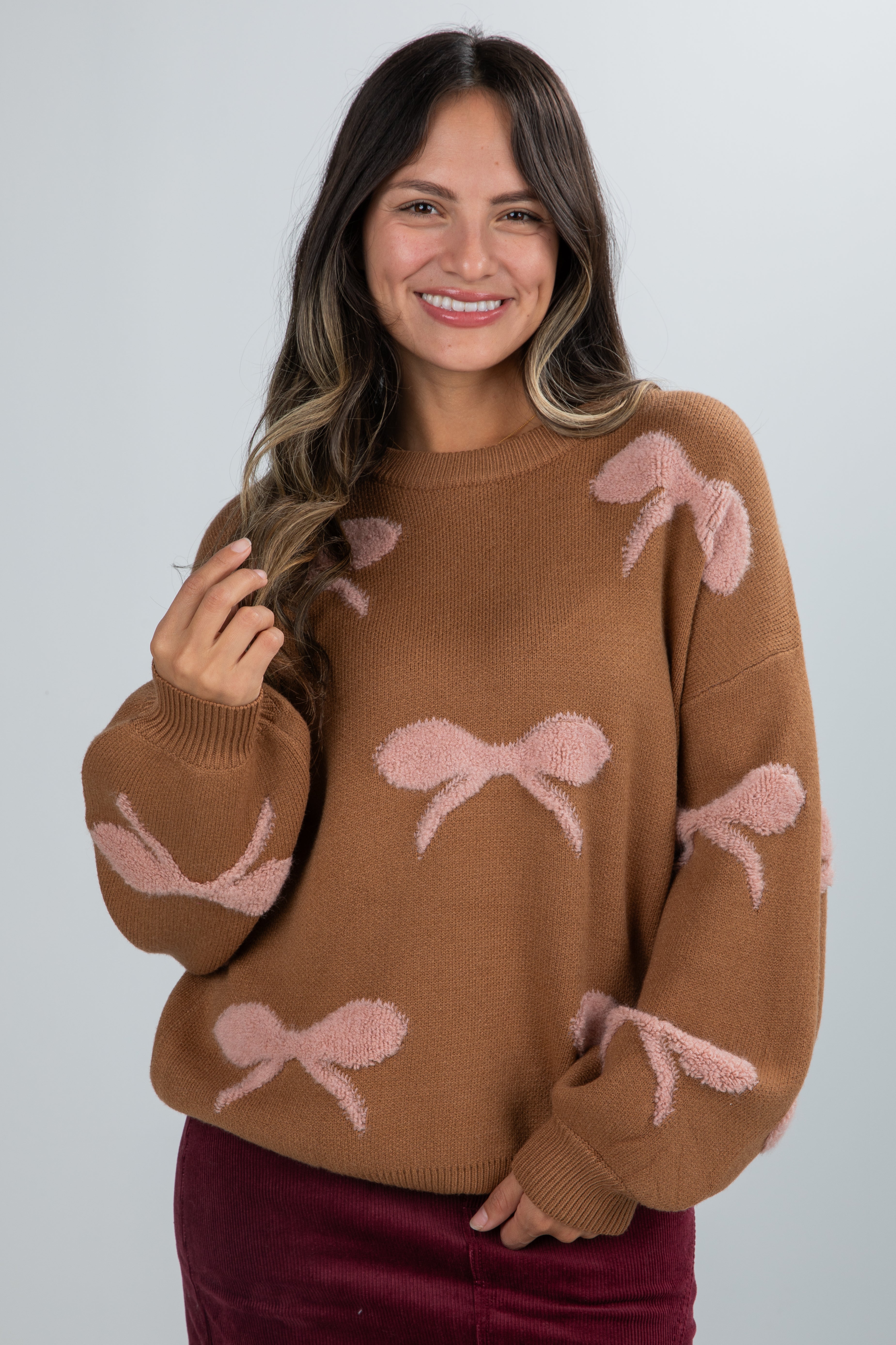 Woman wearing a brown sweater with pink bow patterns on a plain background