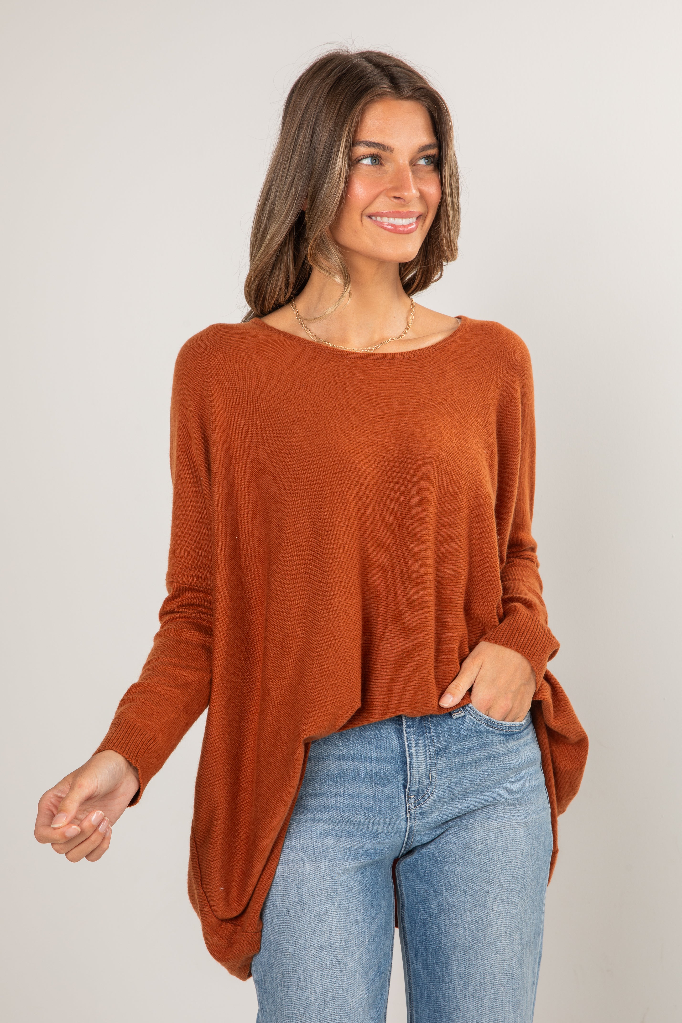 Woman wearing a rust-colored sweater and blue jeans against a plain background
