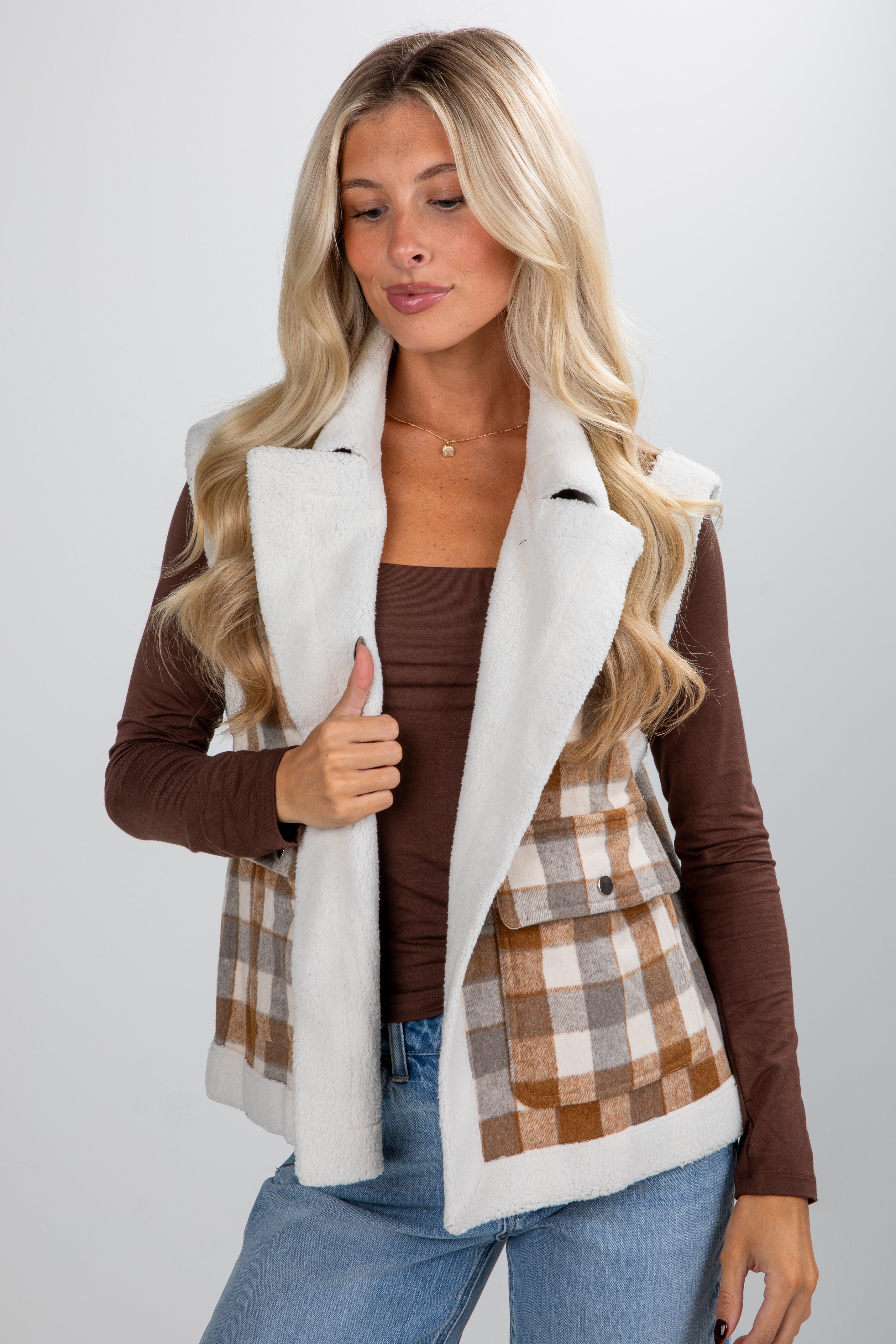 Woman wearing a plaid vest over a brown long-sleeve shirt on a white background