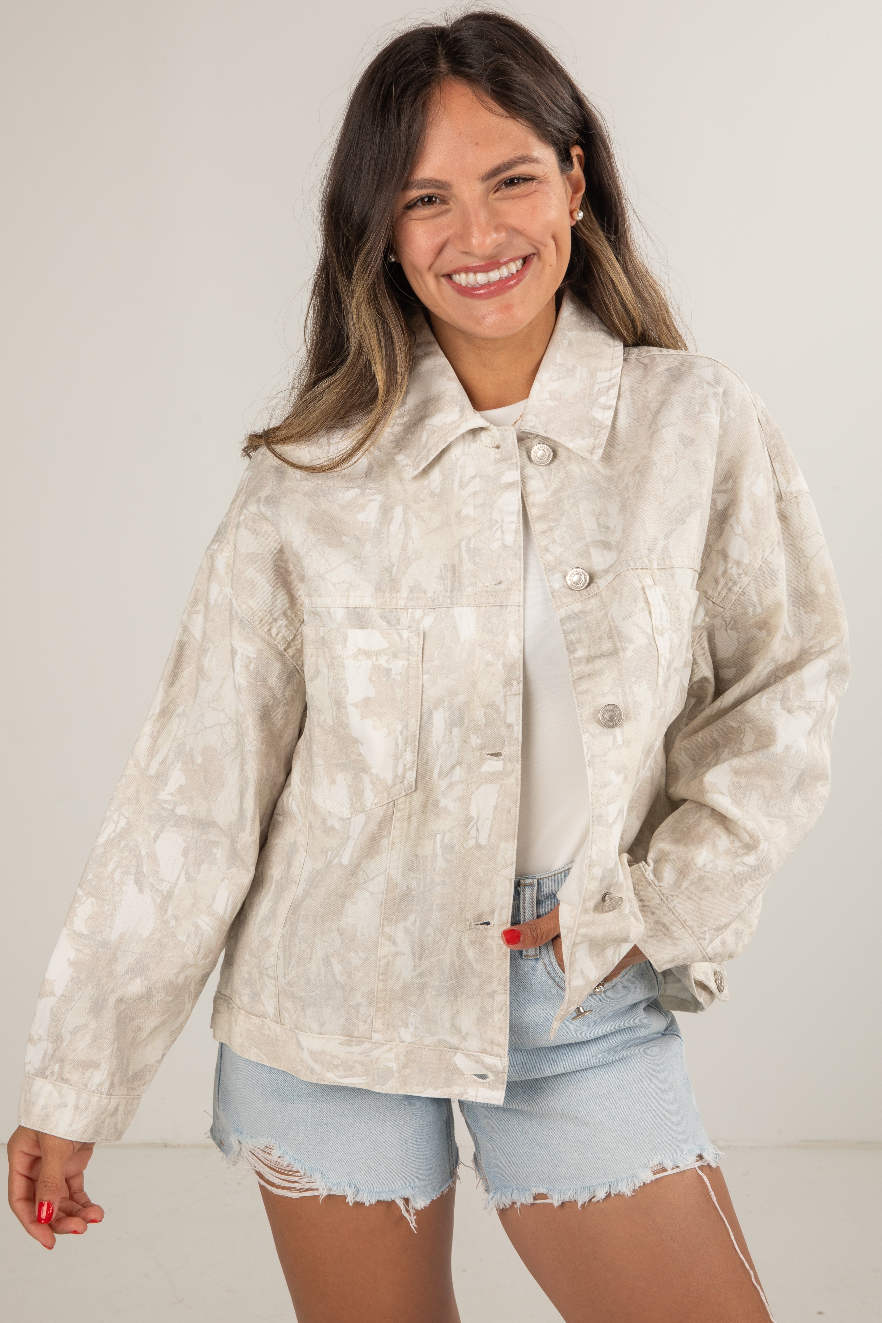 Woman wearing a light-colored jacket and denim shorts on a plain background