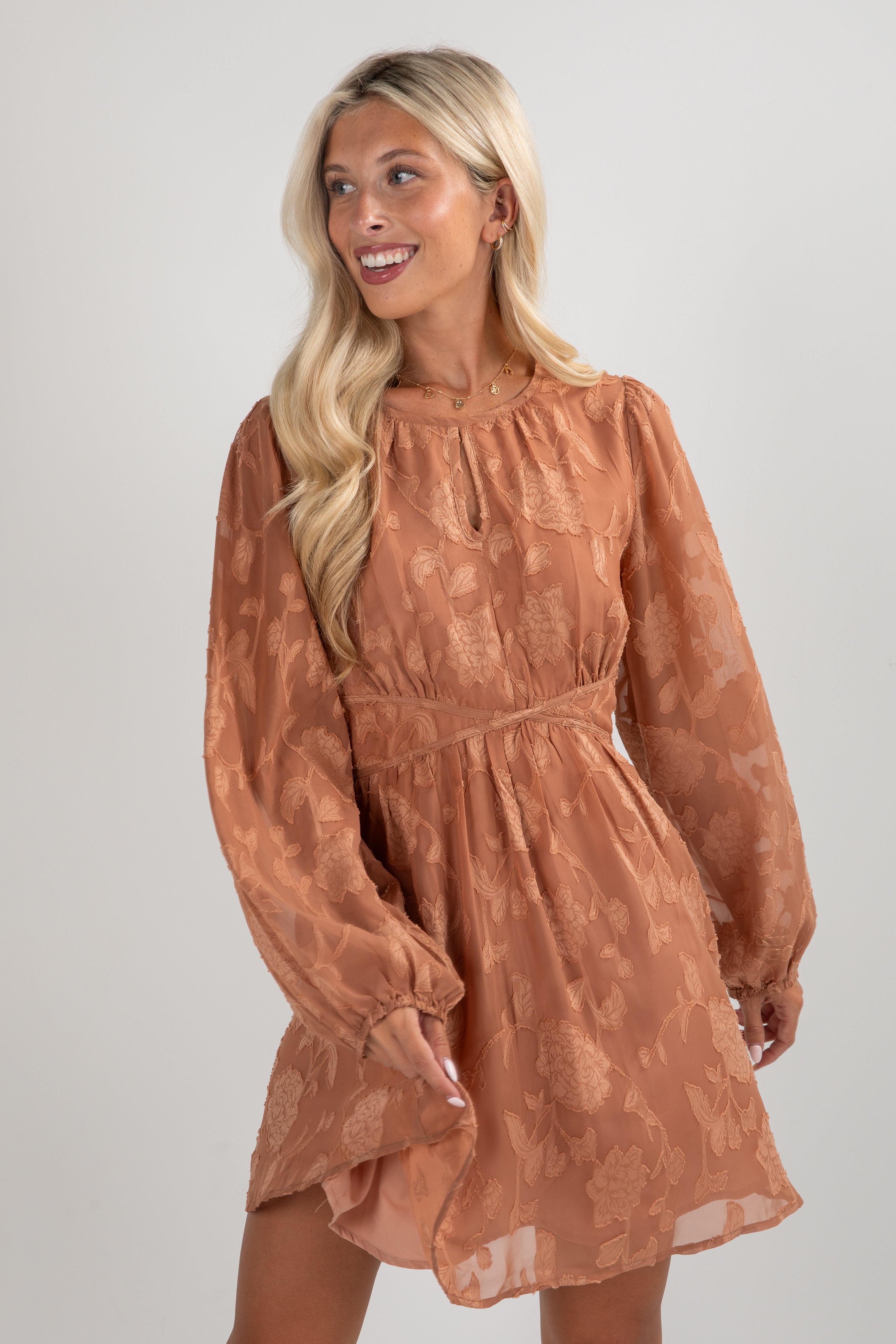 Woman wearing a brown dress with long sleeves against a plain background