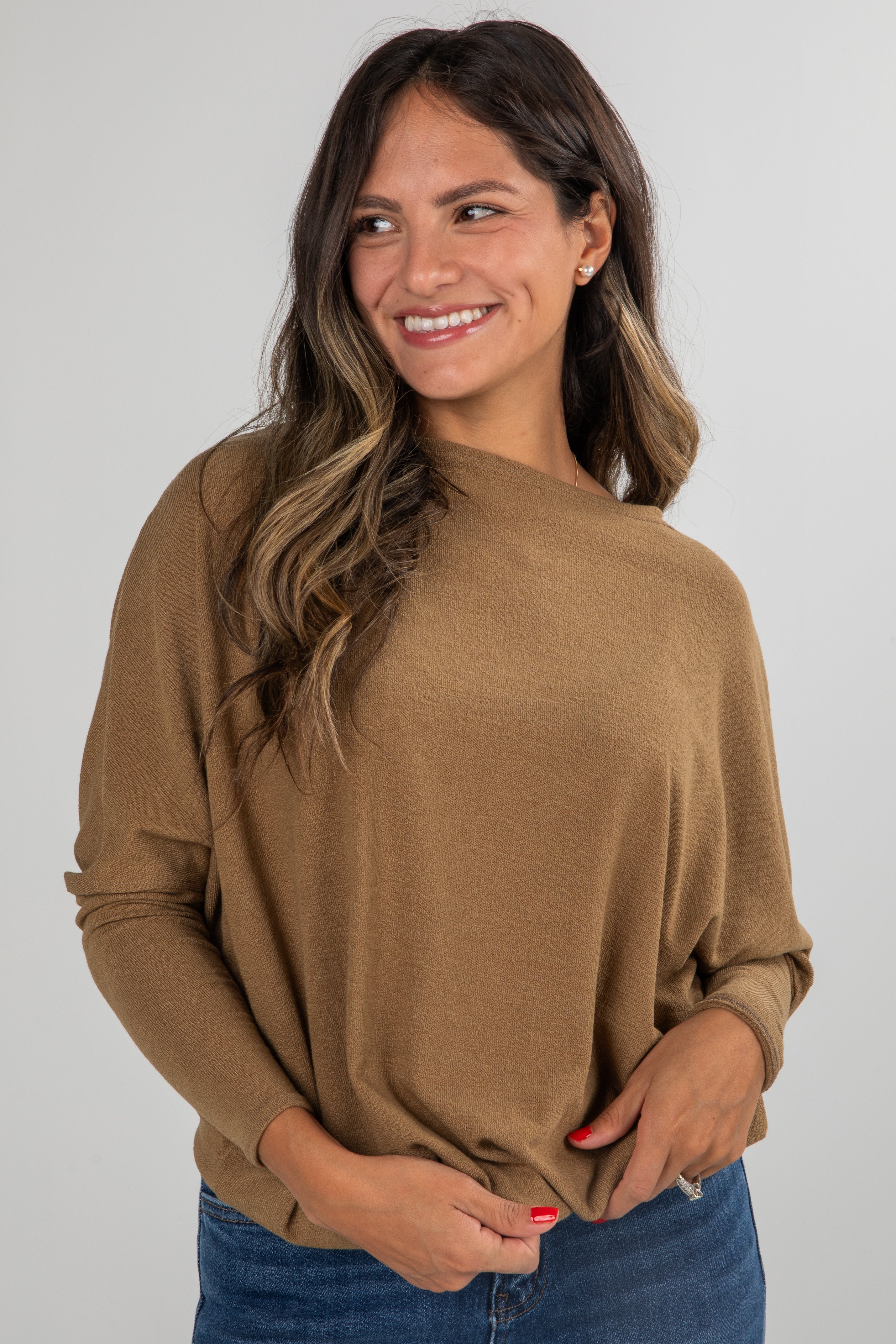 Woman wearing a brown sweater and blue jeans against a plain background