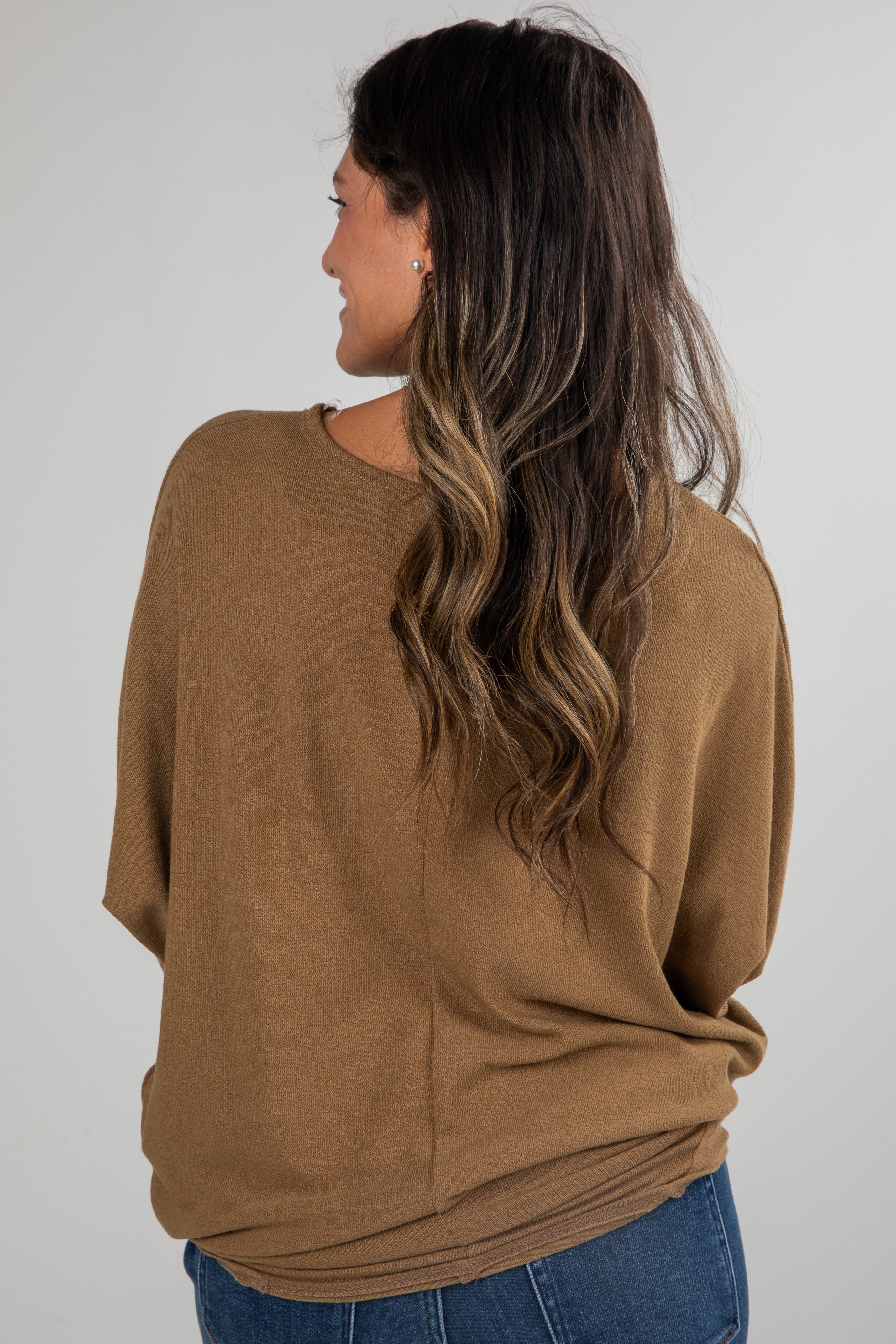 Woman wearing a brown sweater and blue jeans against a white background