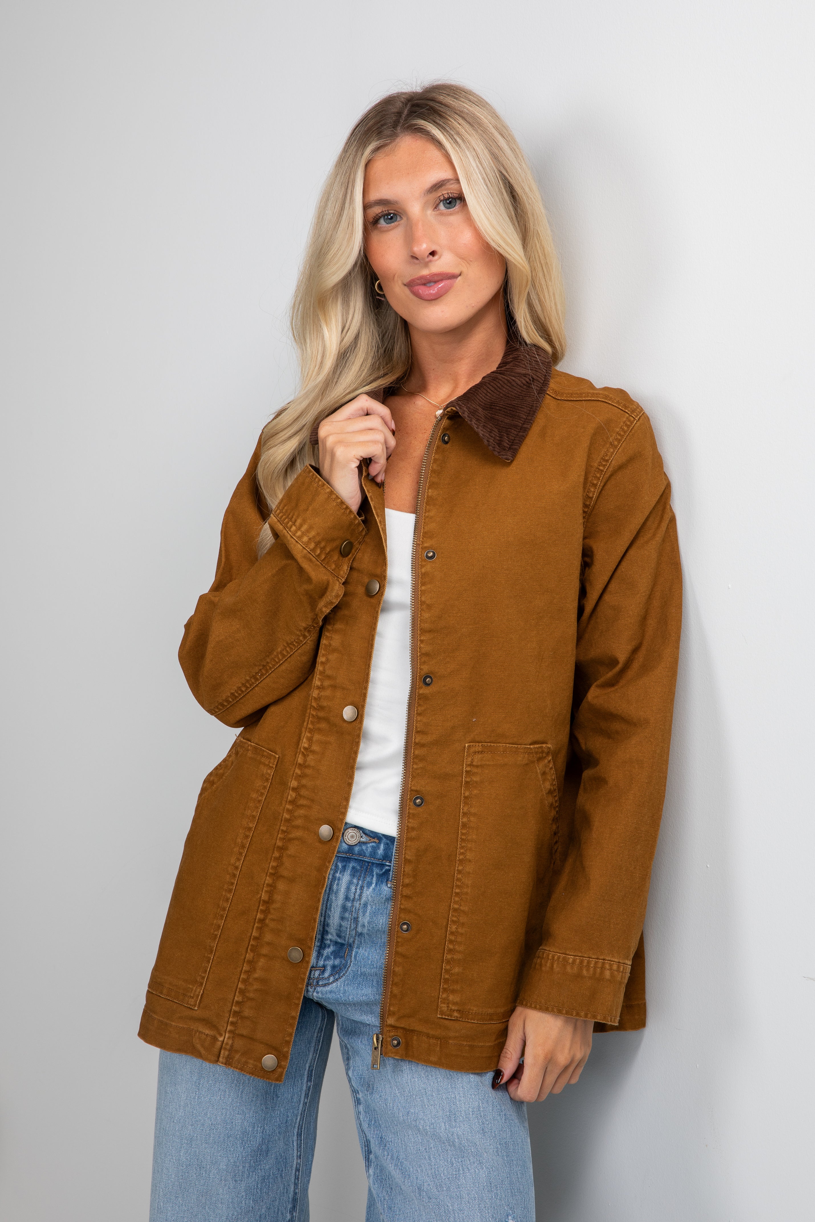 Woman wearing a brown jacket and blue jeans against a plain background