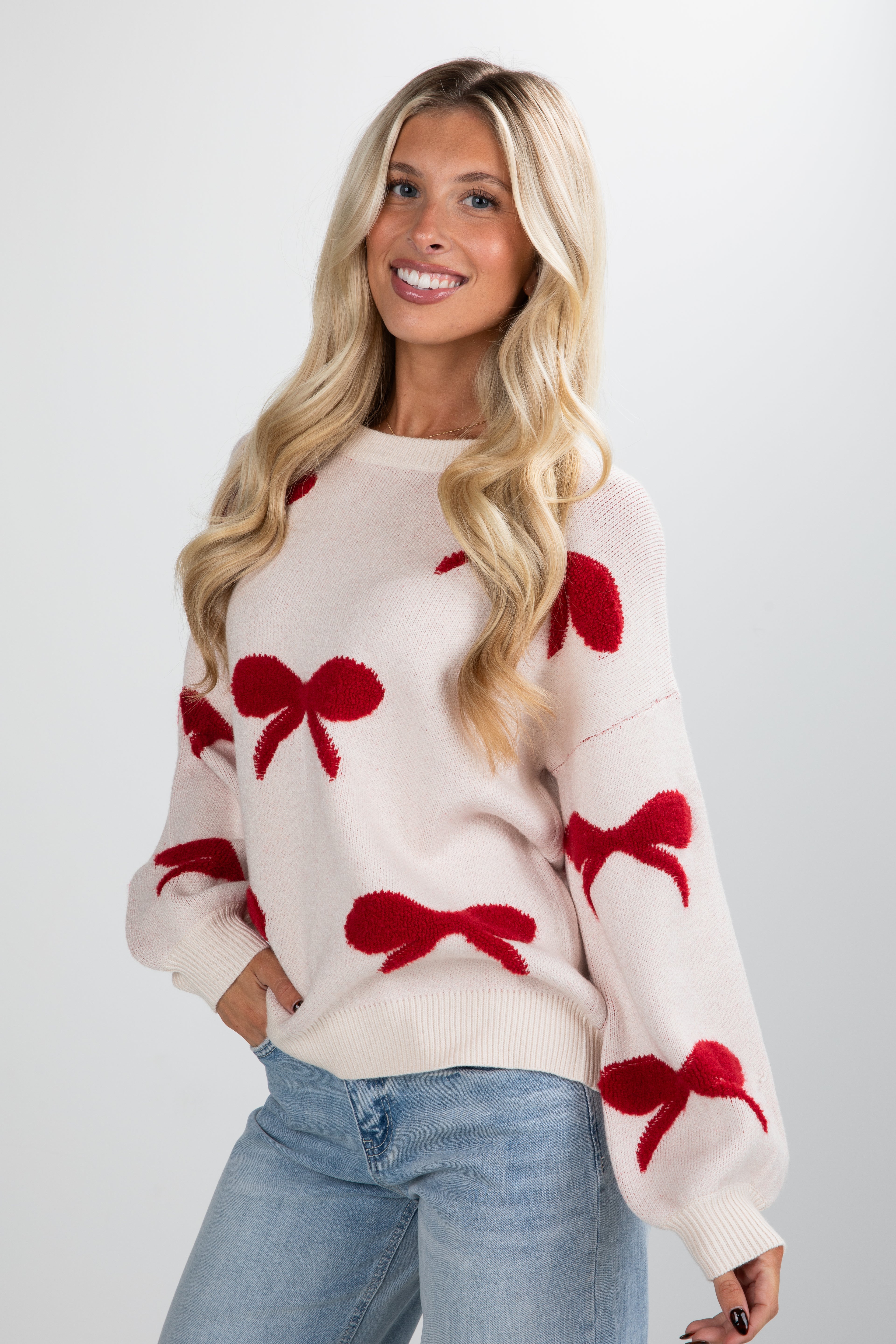 Woman wearing a cream sweater with red bow patterns on a white background