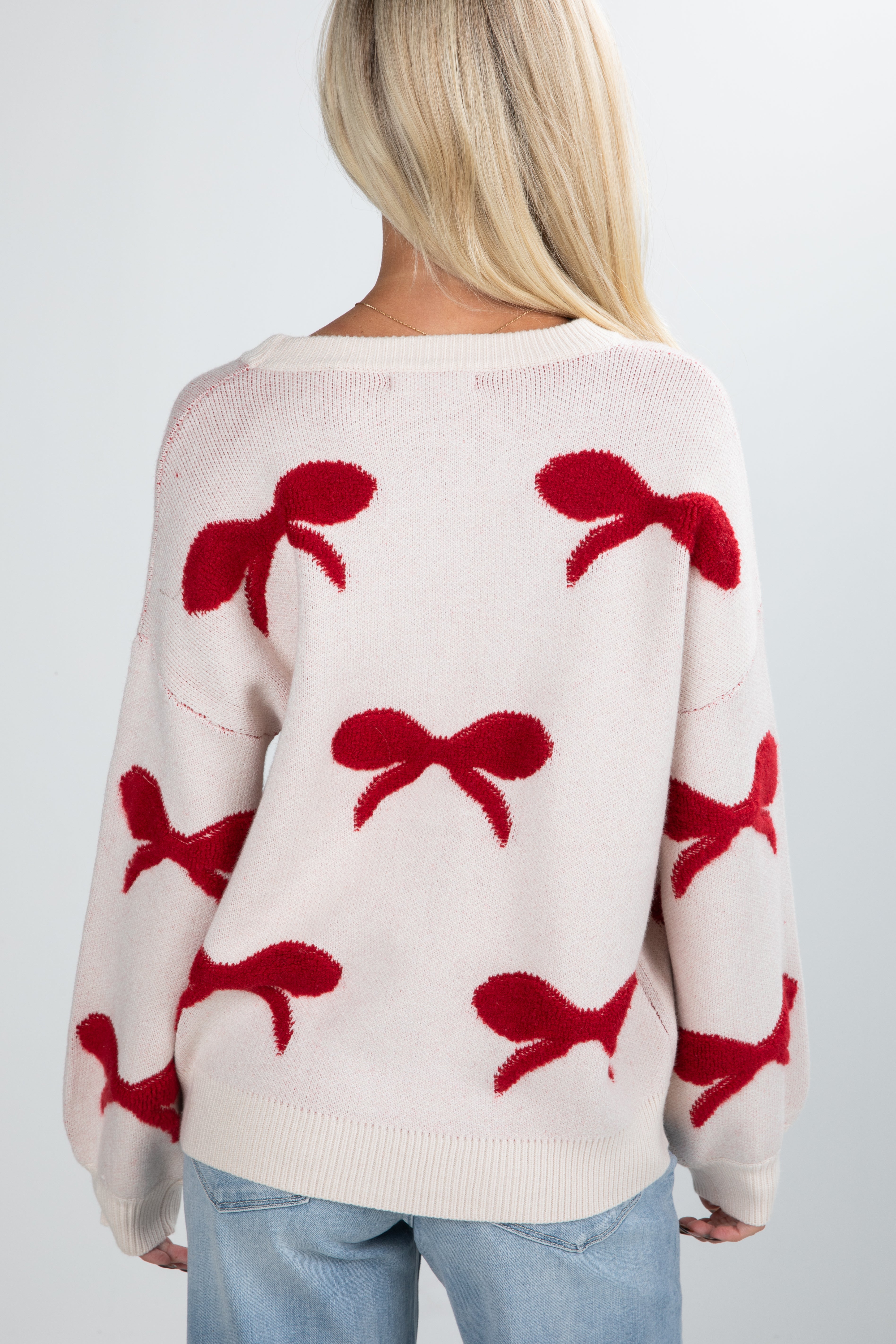 Person wearing a cream sweater with red bow patterns on a plain background