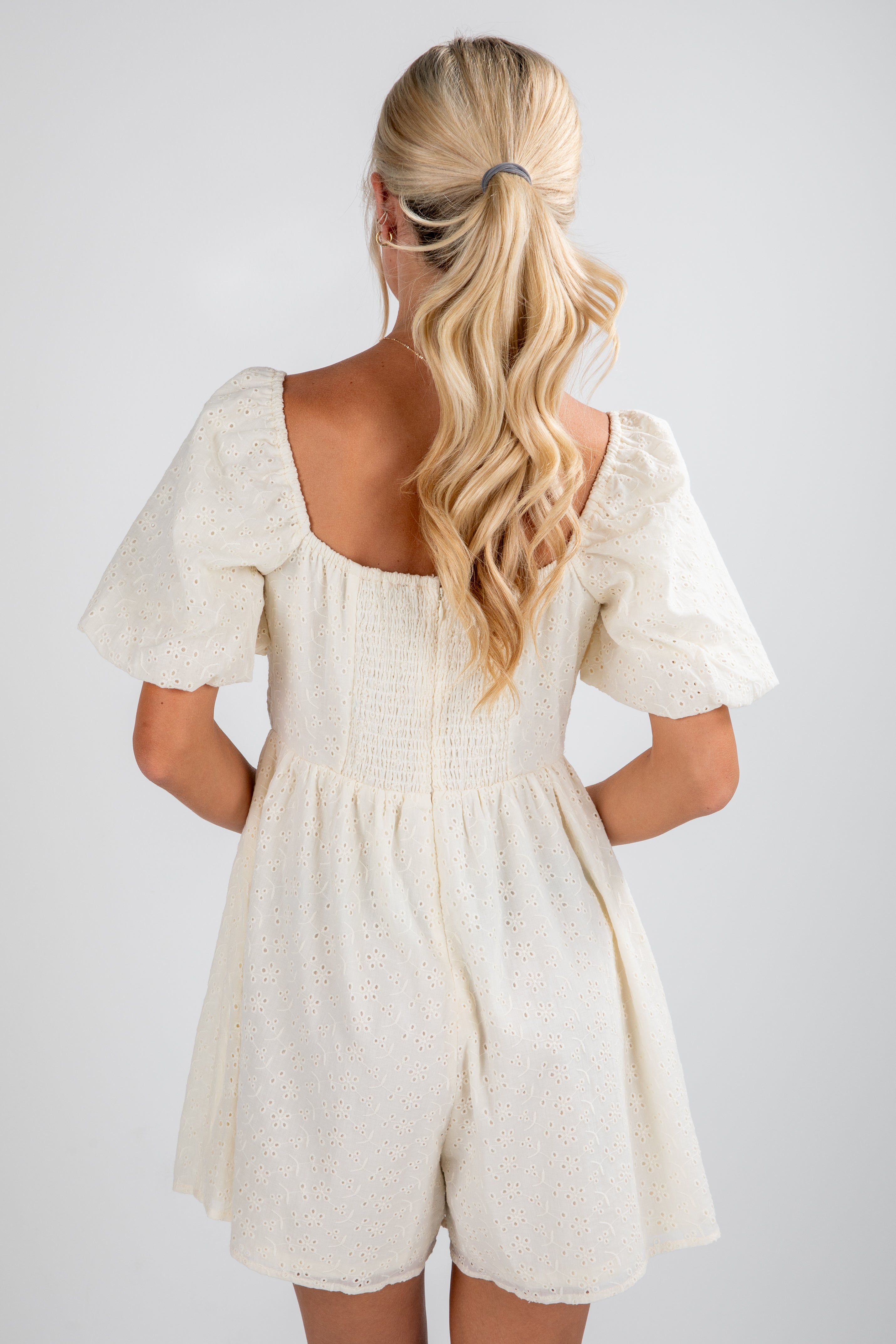 Woman wearing a white romper with puffed sleeves on a plain background