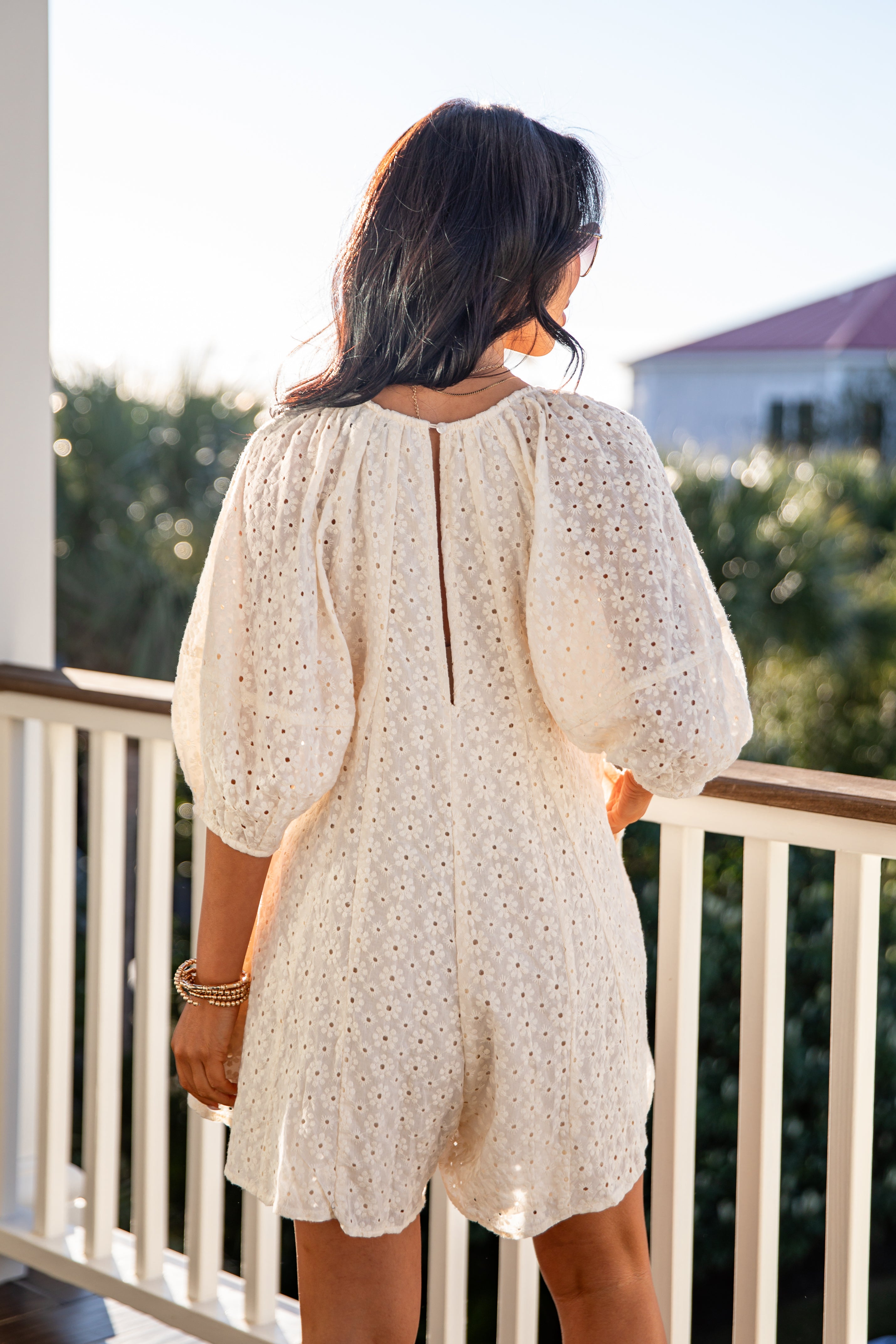 Woman wearing a white lace dress standing on a balcony with a scenic background