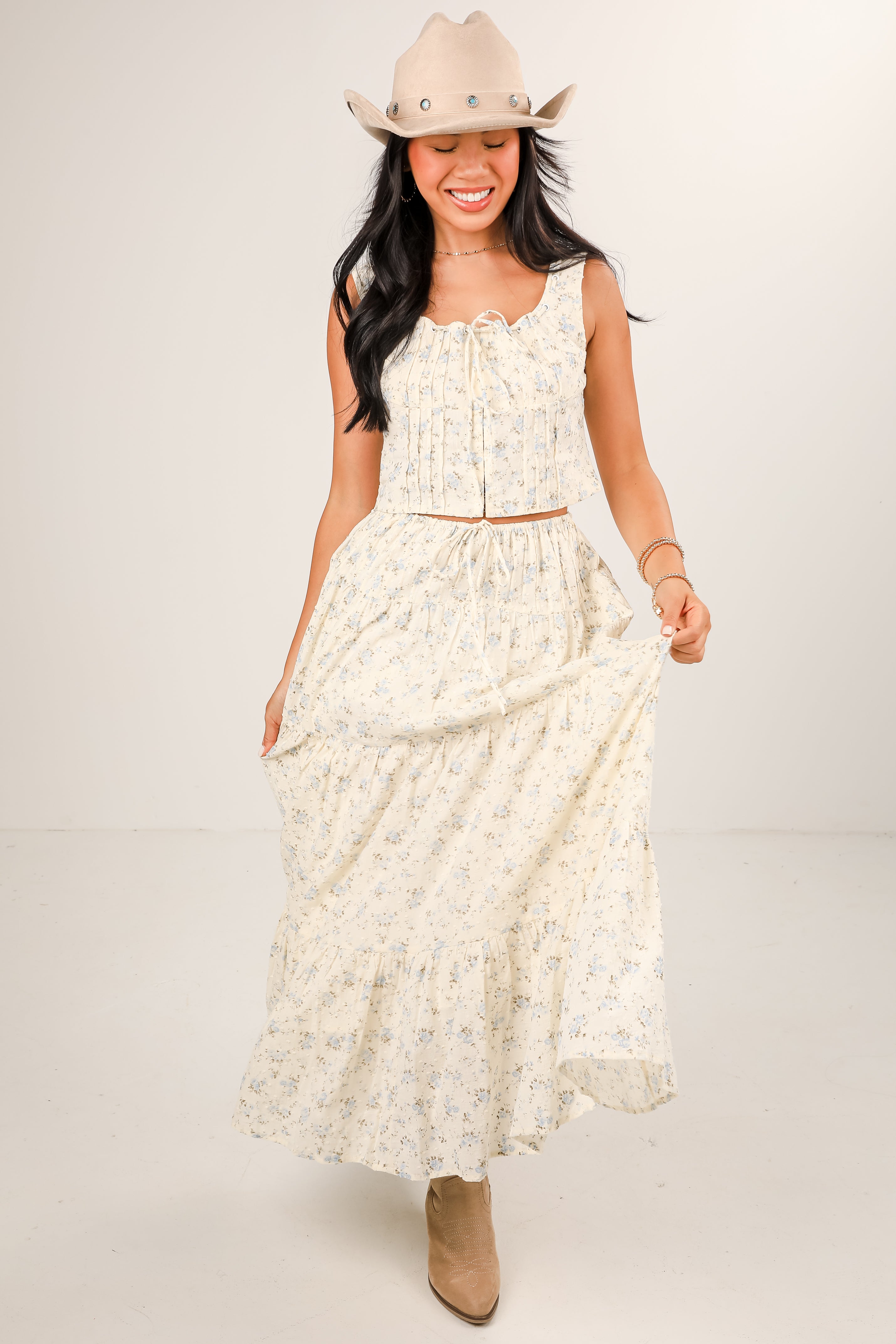 Woman wearing a white floral dress and cowboy hat on a plain background