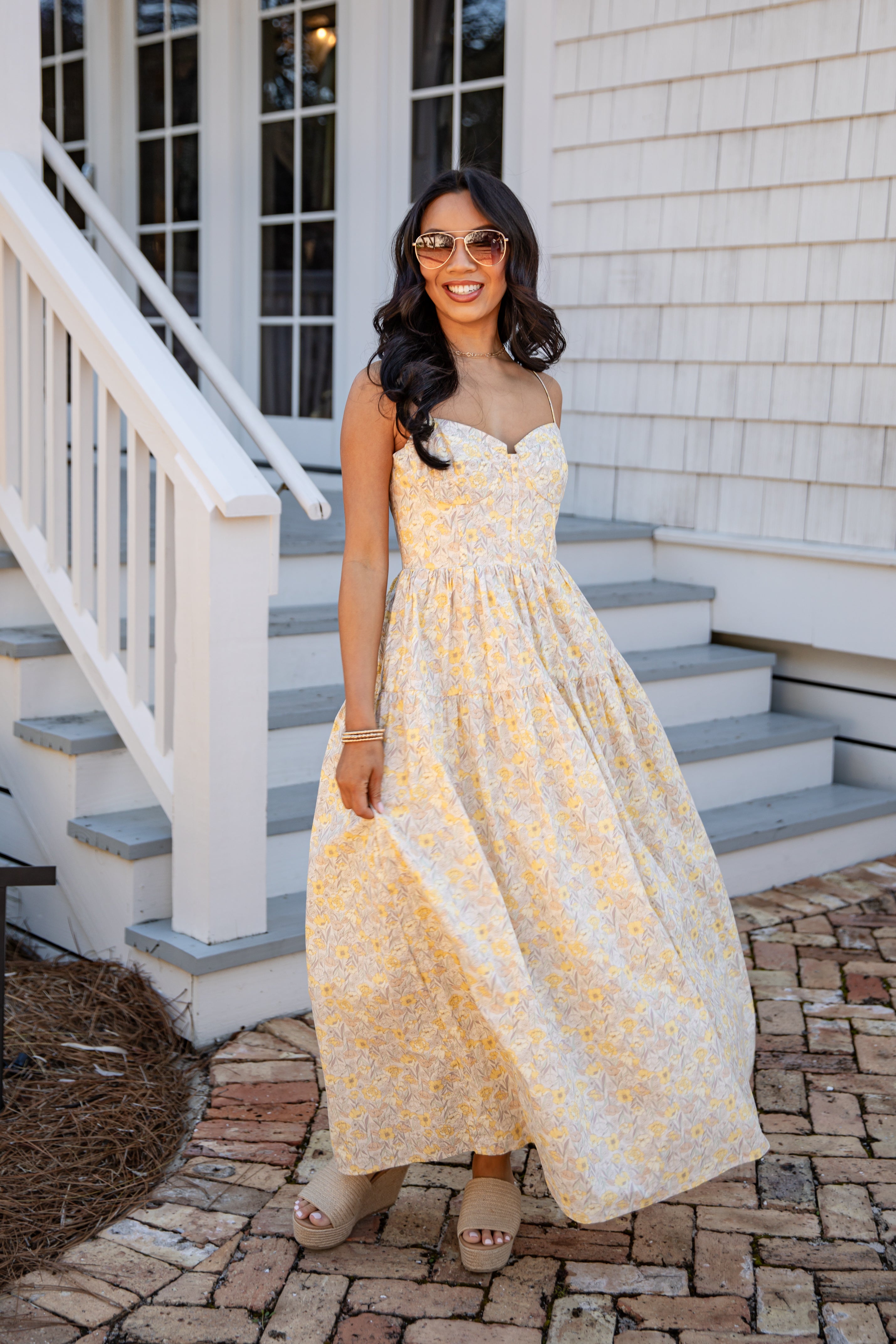 Woman in a yellow floral dress standing on a staircase outside a house.