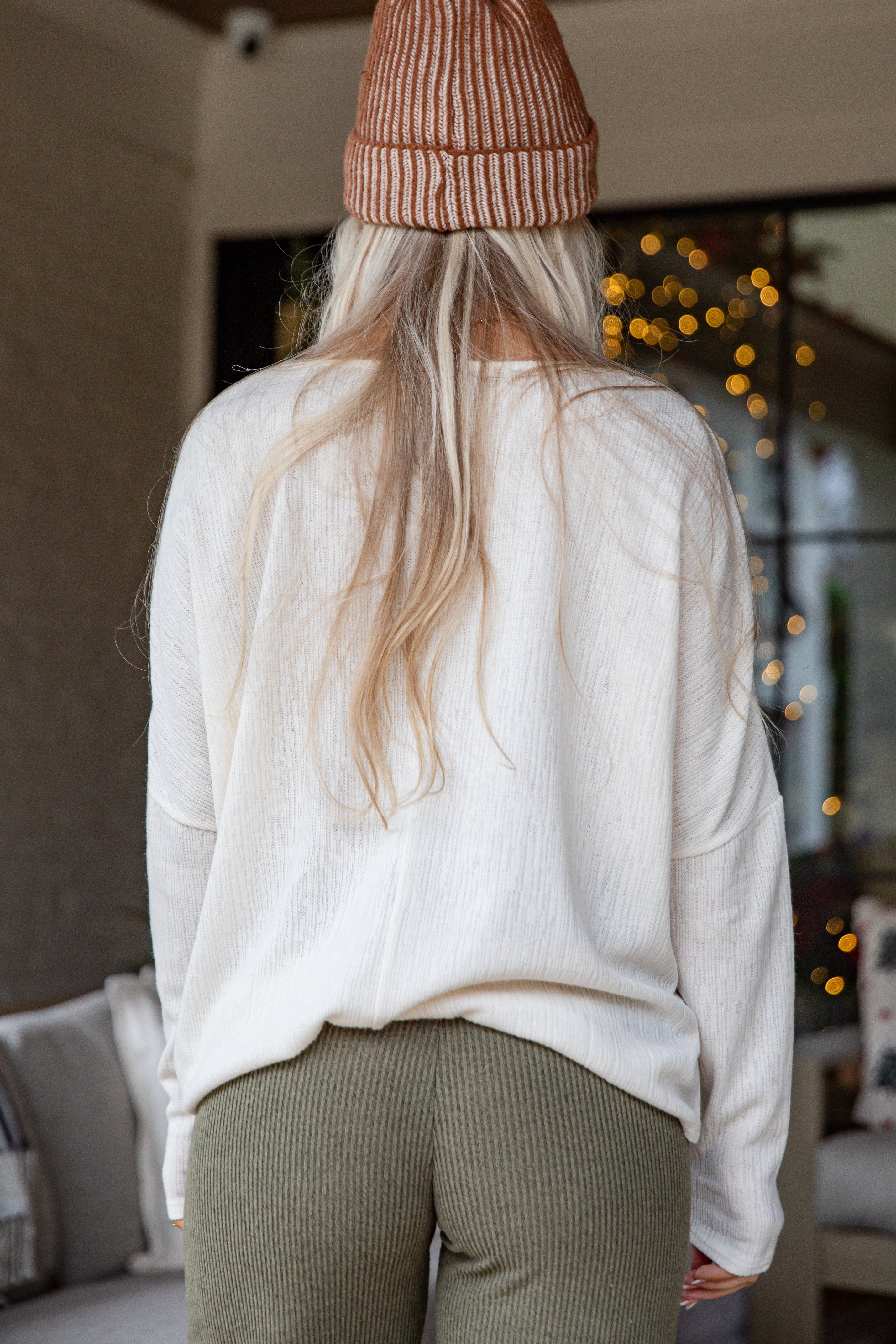 Person wearing a white sweater and brown beanie in a cozy indoor setting