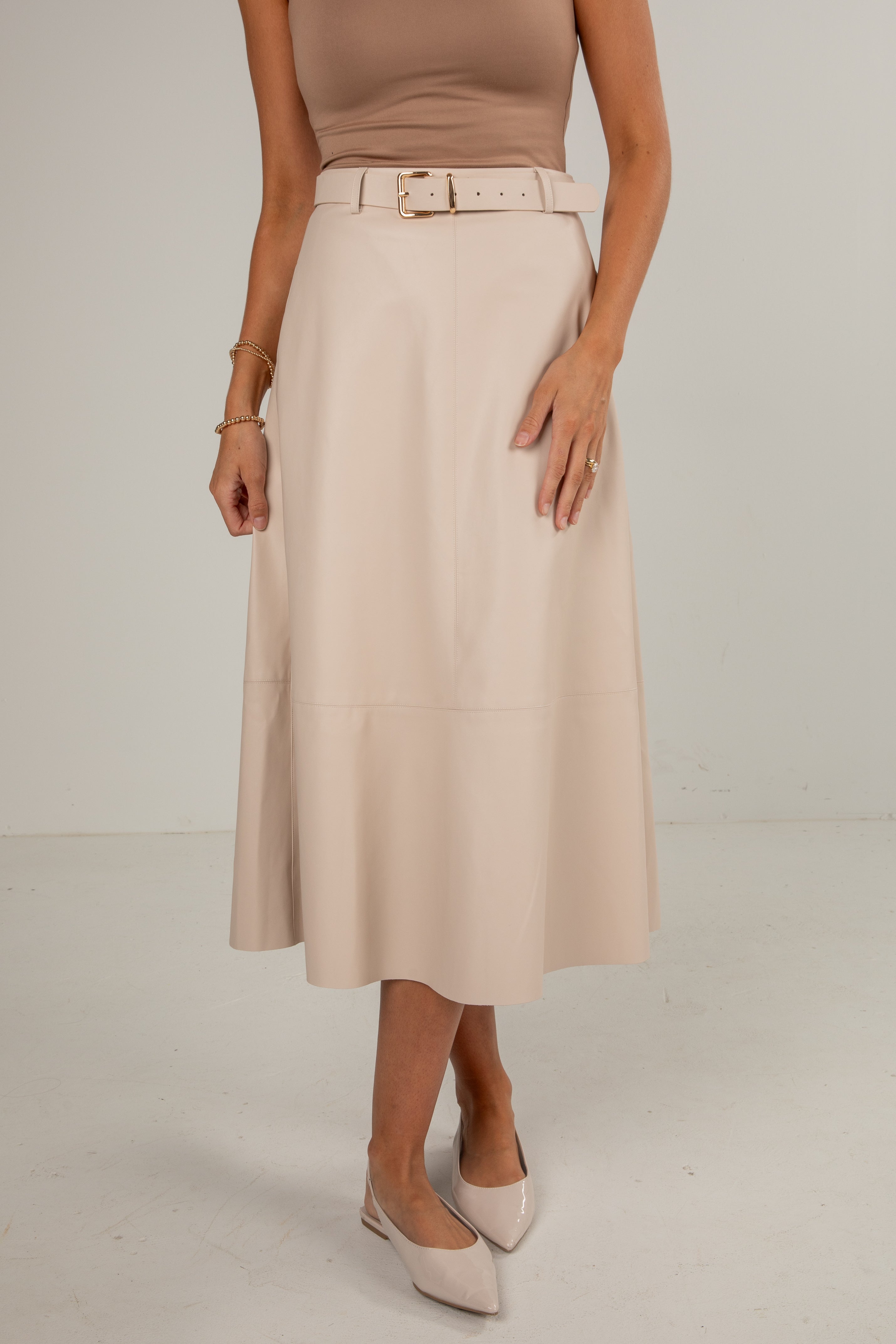 Person wearing a beige skirt with a belt on a plain background