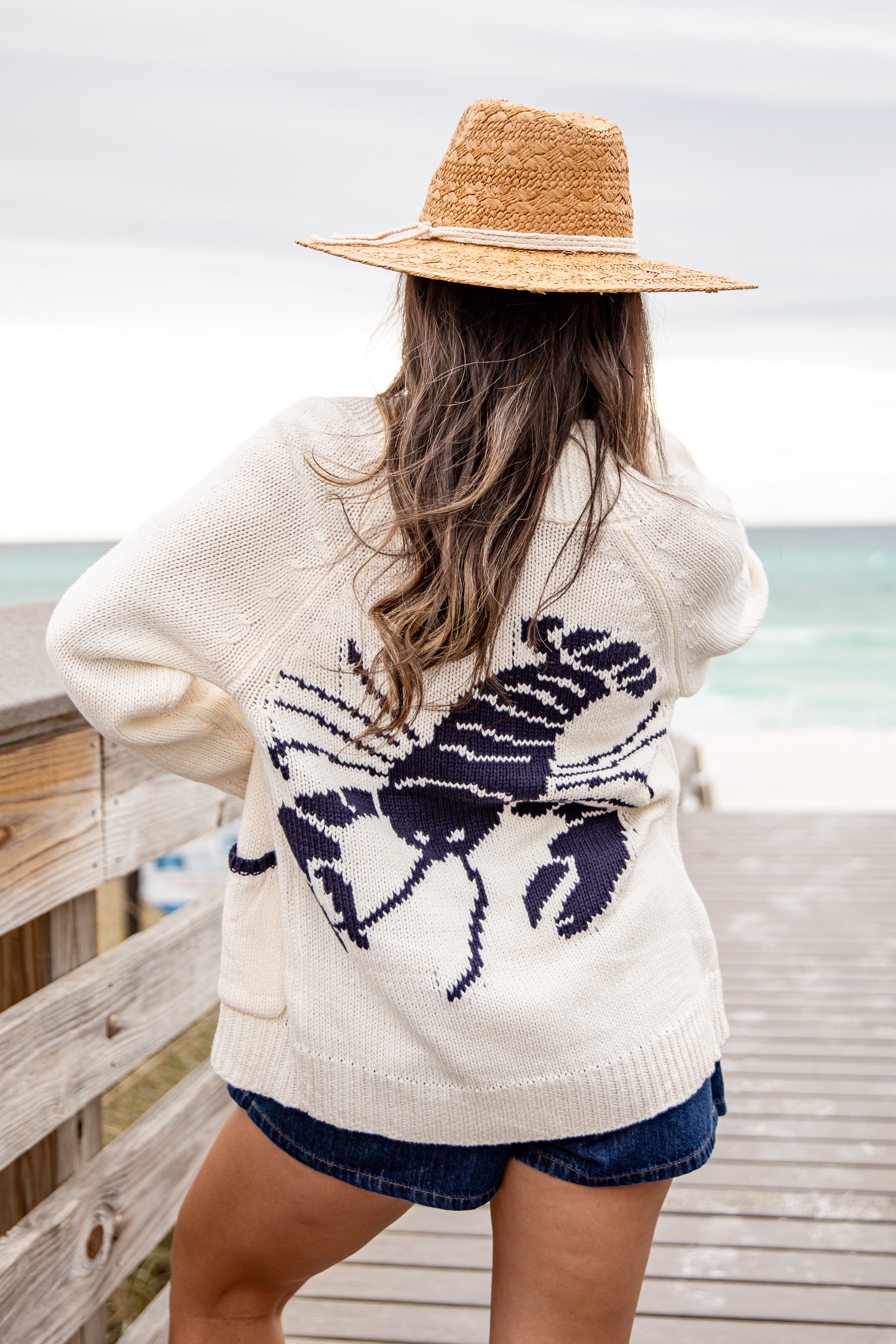 Person wearing a cream cardigan with a crab pattern by the ocean