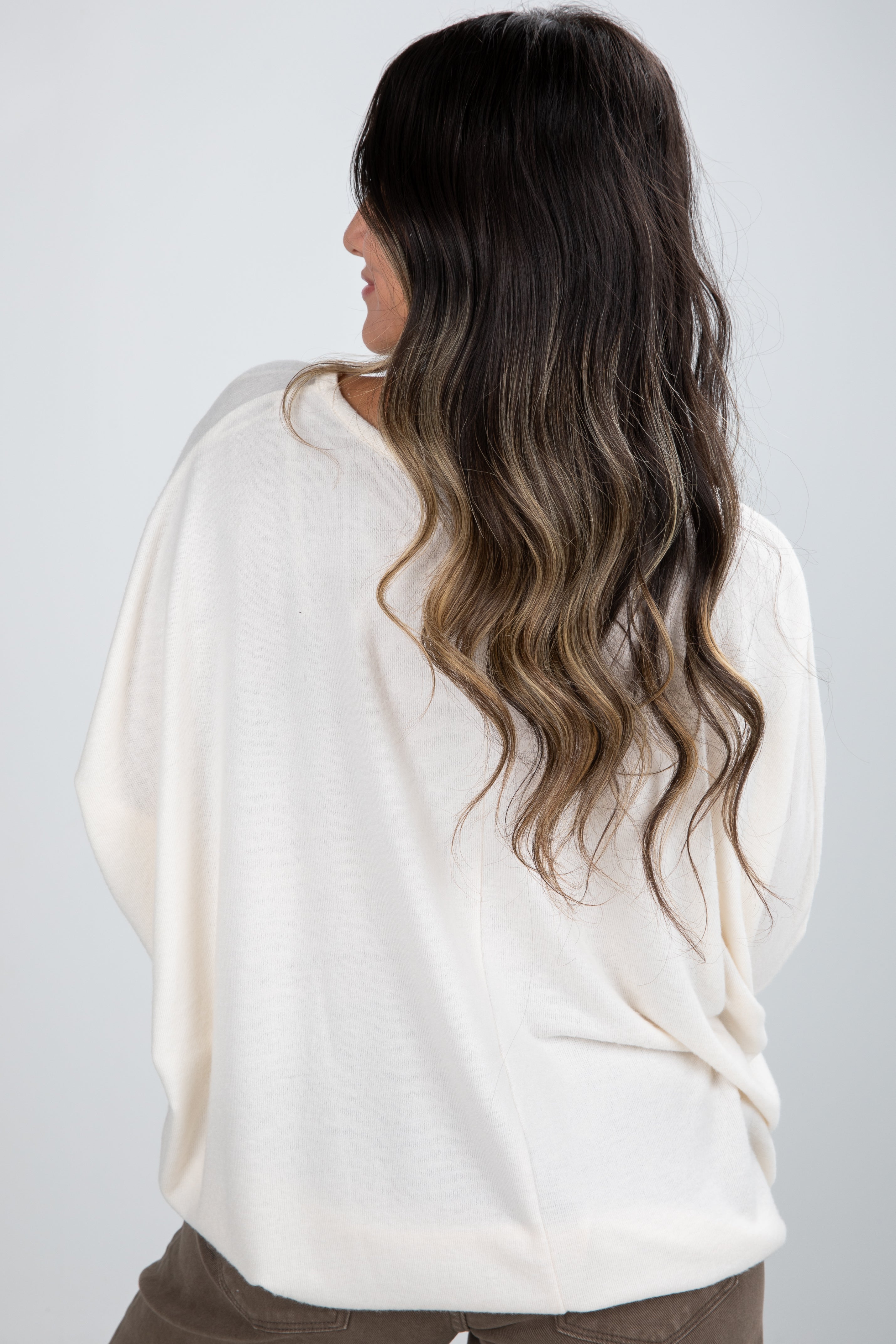 Person wearing a white sweater with long, wavy hair on a plain background