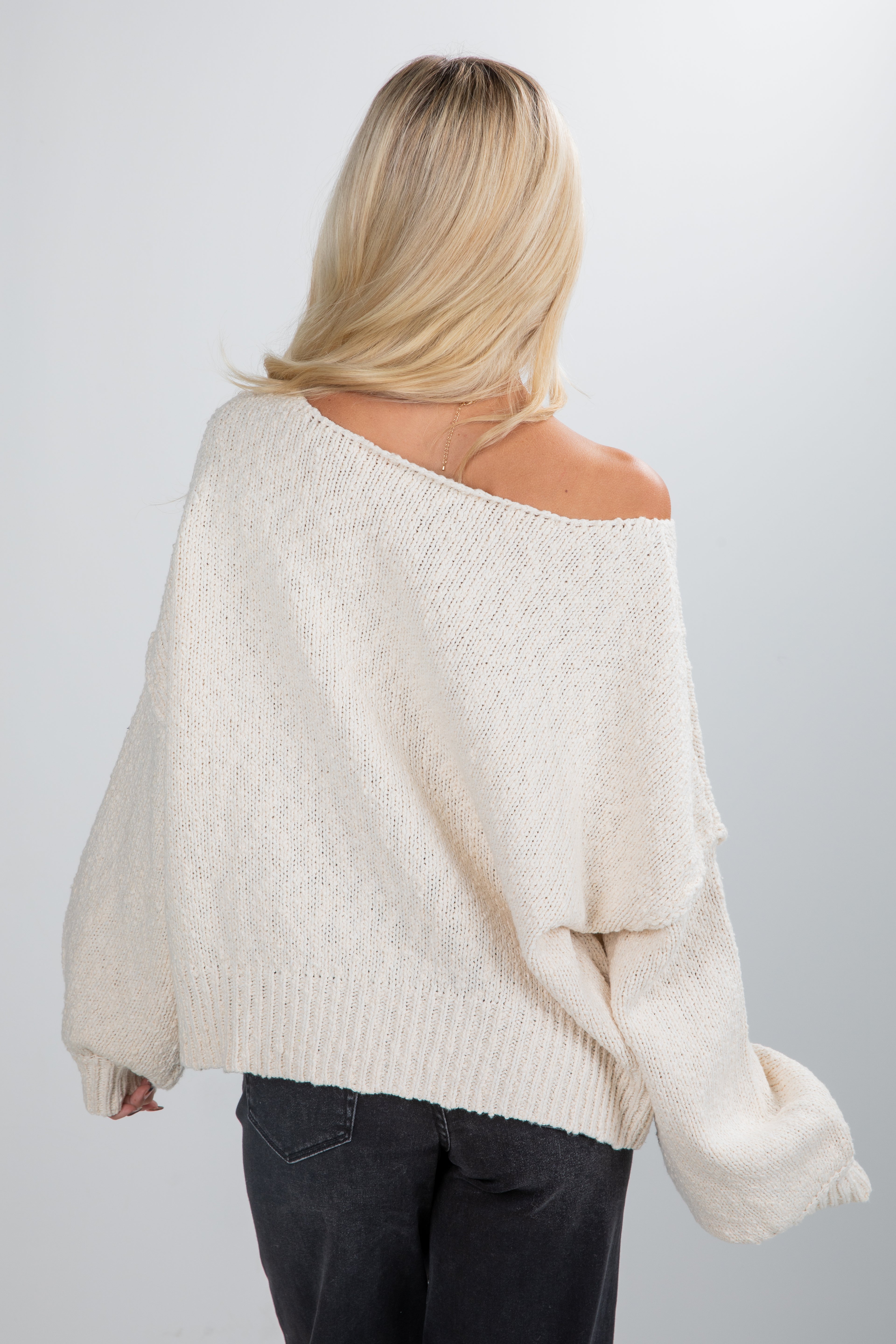 Person wearing a cream off-shoulder sweater against a plain background