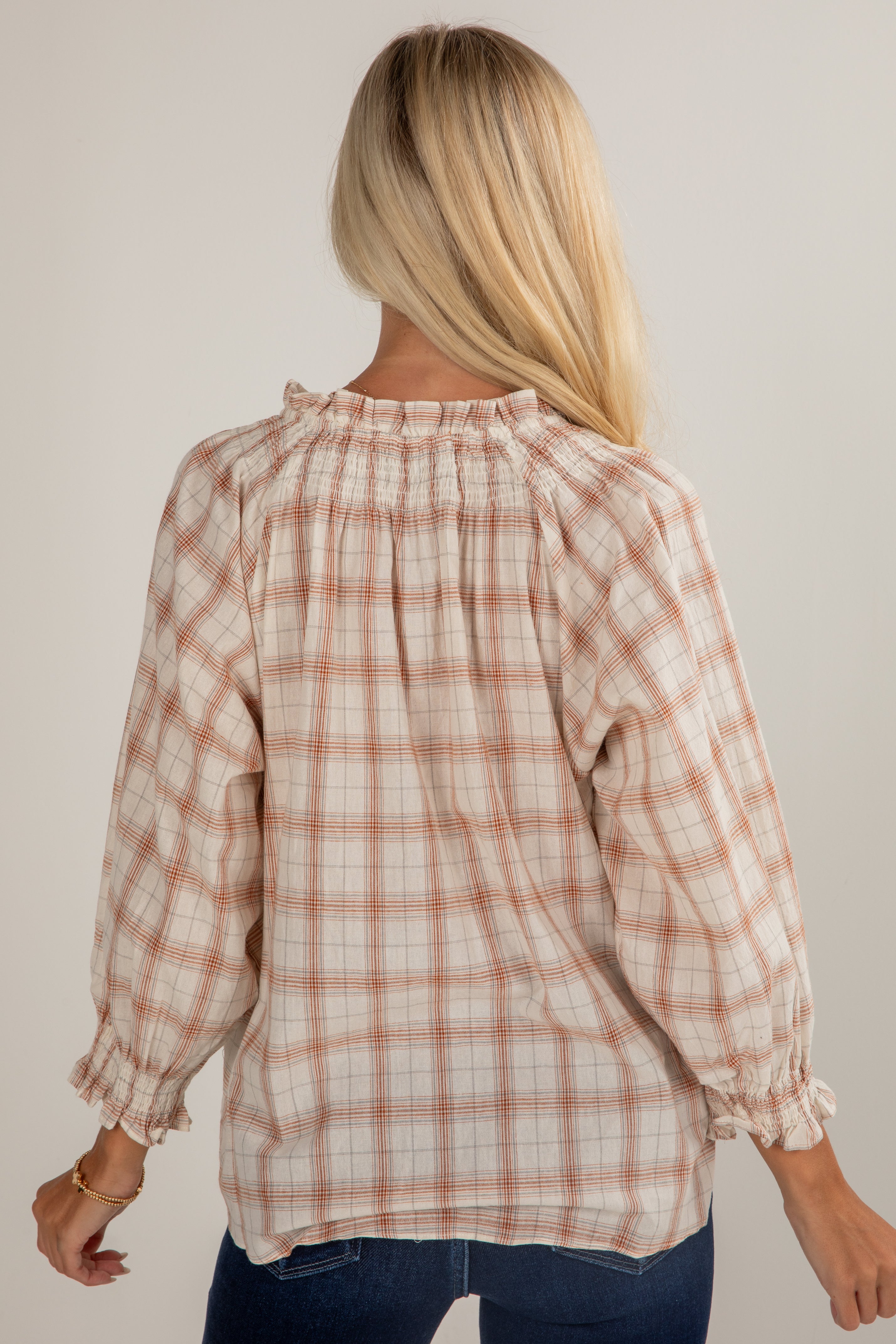Person wearing a plaid blouse with long sleeves against a plain background