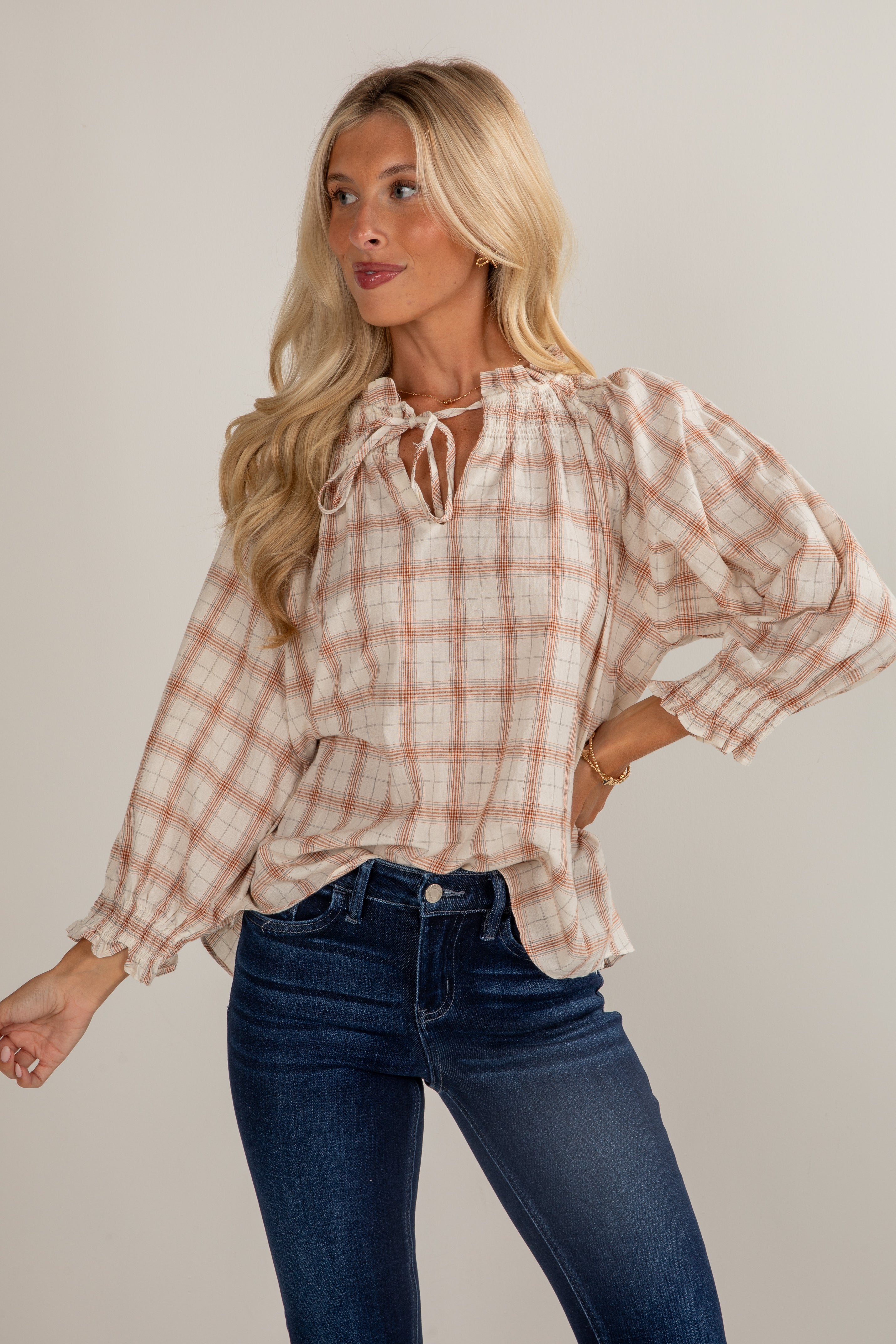 Woman wearing a plaid blouse and jeans against a plain background
