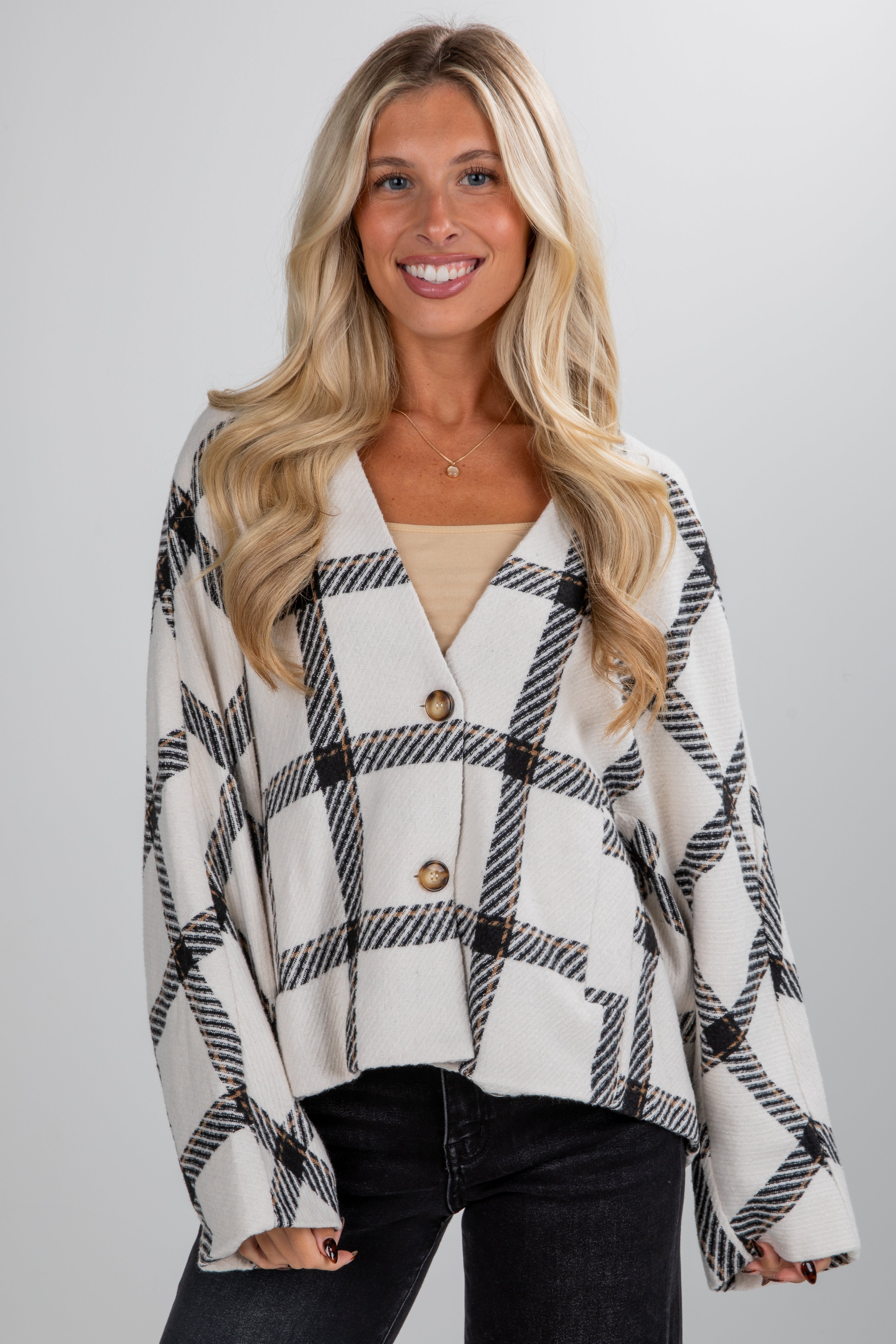 Woman wearing a plaid cardigan over a beige top on a plain background