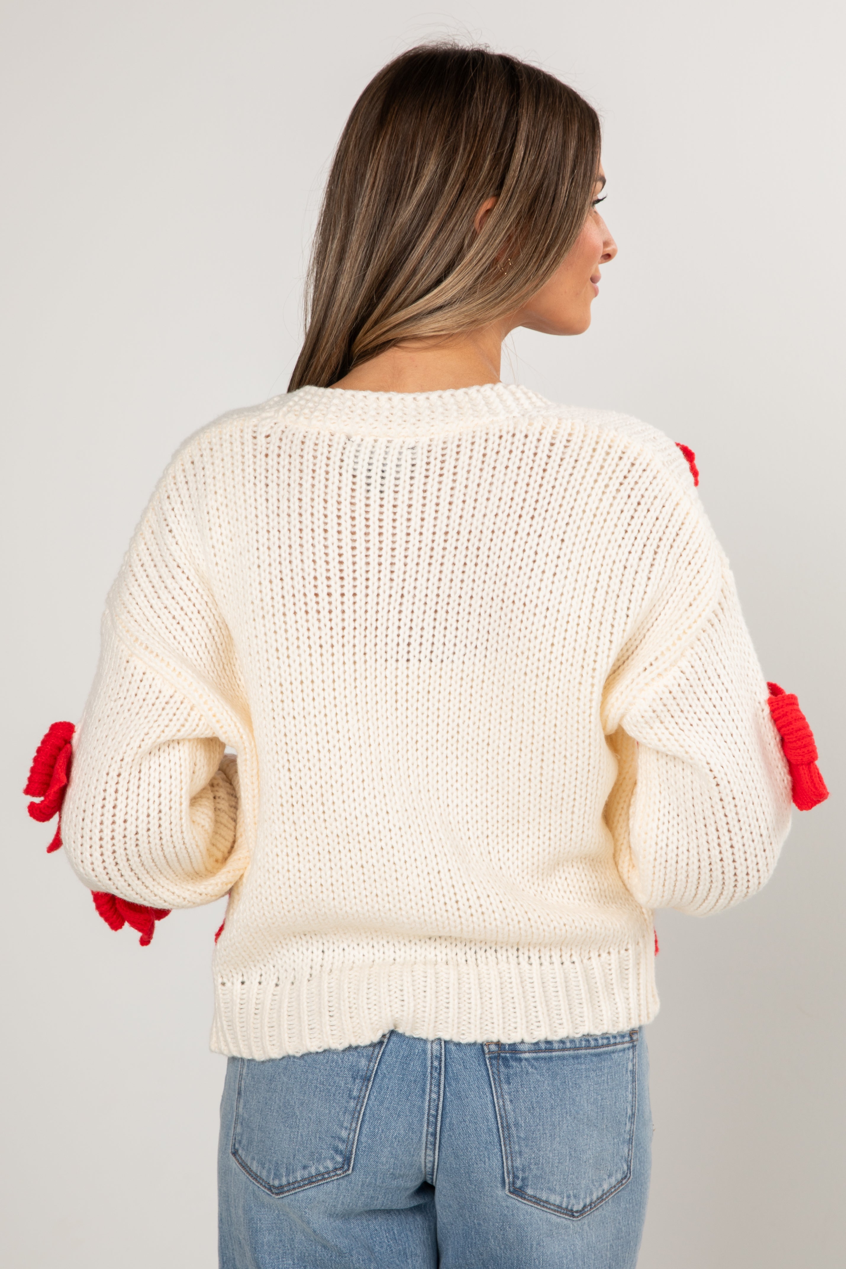 Woman wearing a cream sweater with red accents on a plain background