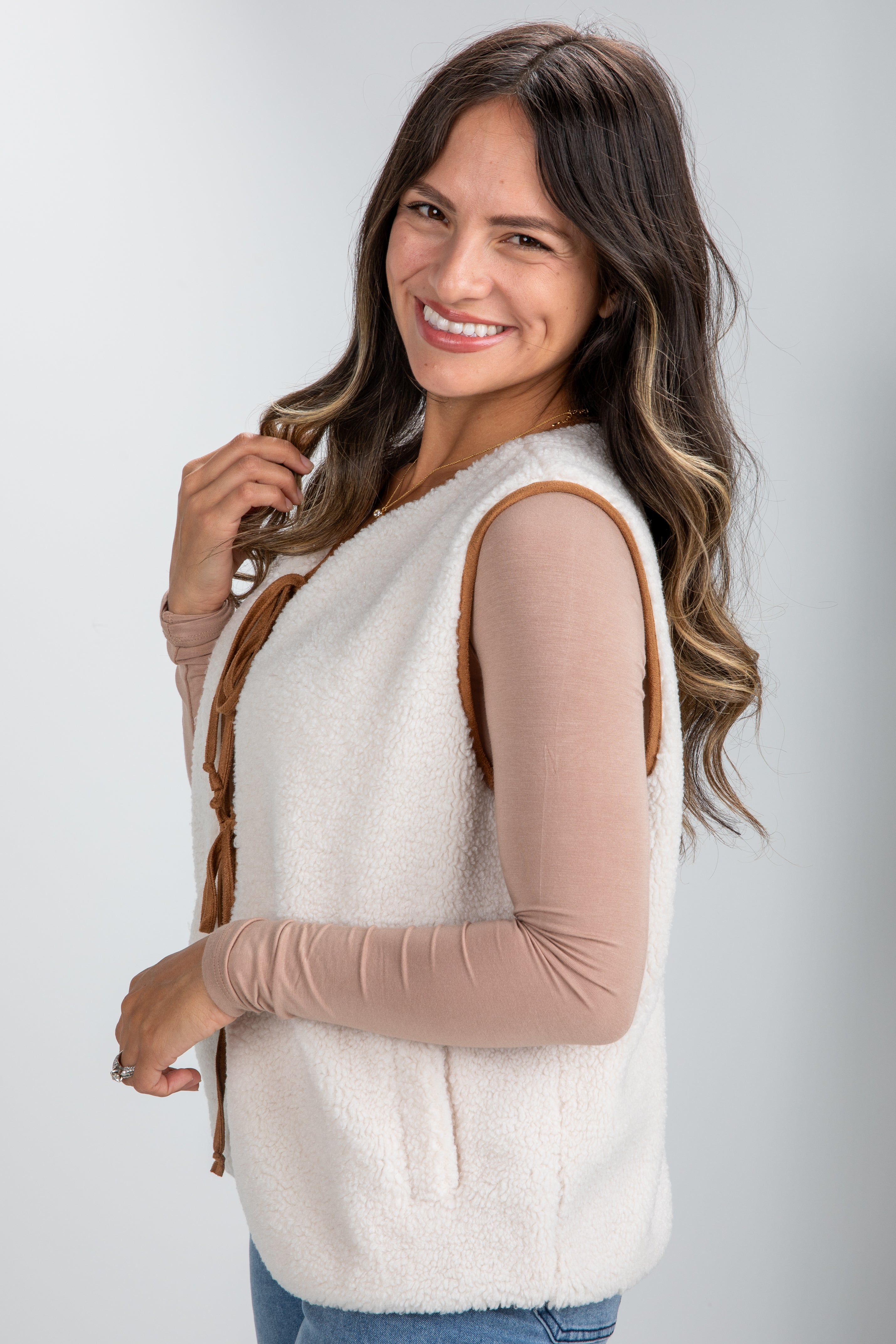 Woman wearing a white vest over a beige long-sleeve shirt on a plain background