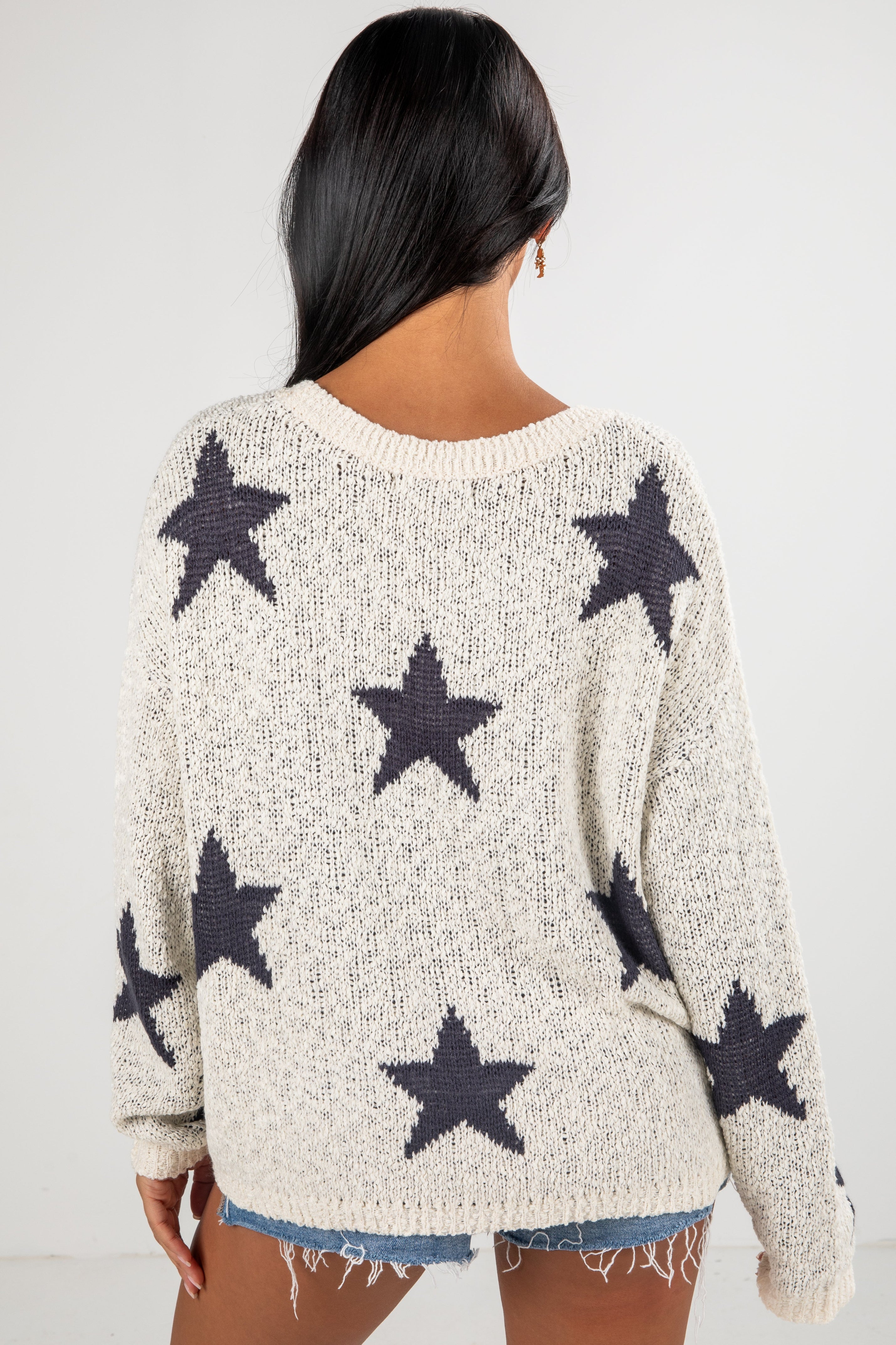 Person wearing a cream sweater with black star patterns on a white background