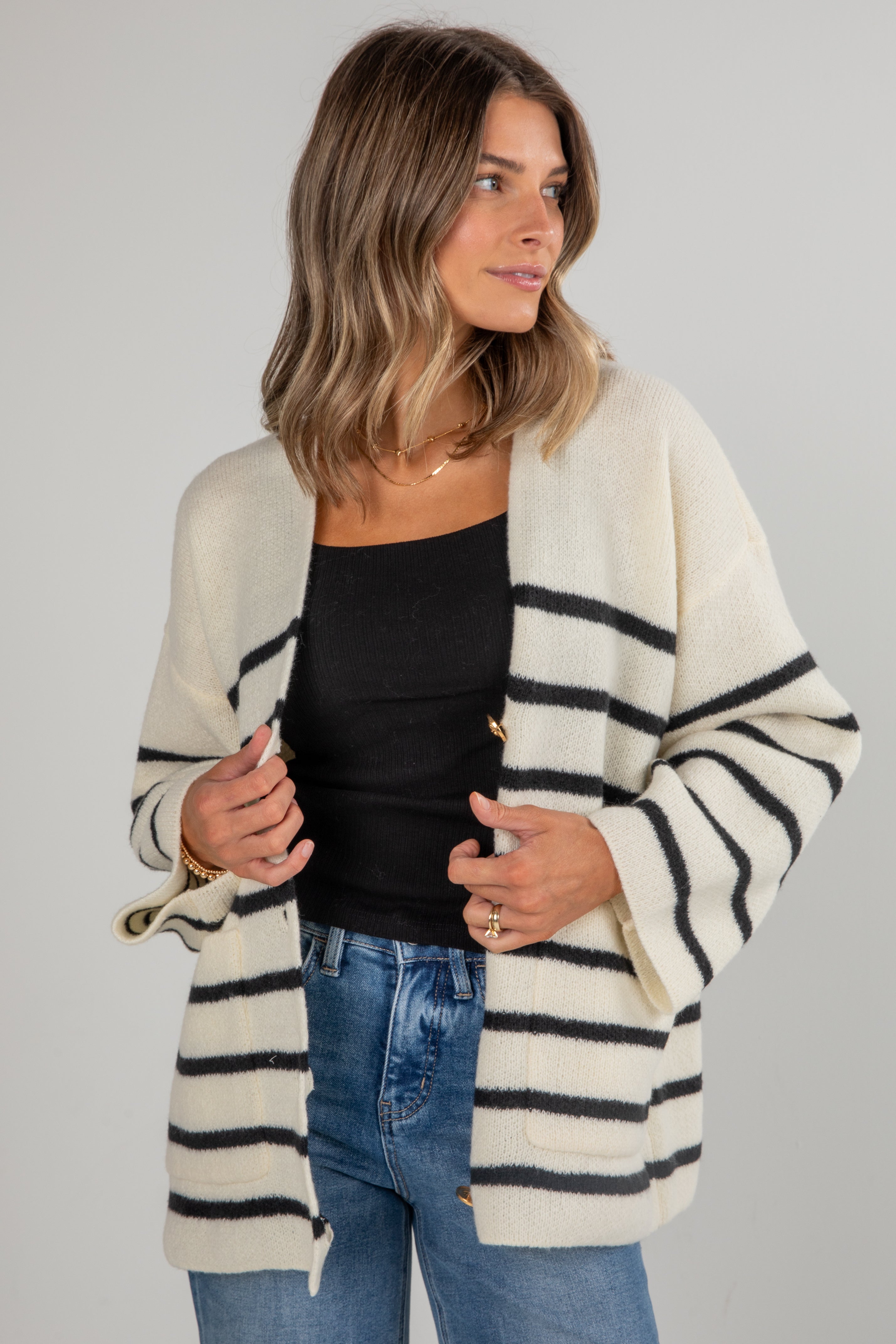 Woman wearing a striped cardigan over a black top and blue jeans on a gray background