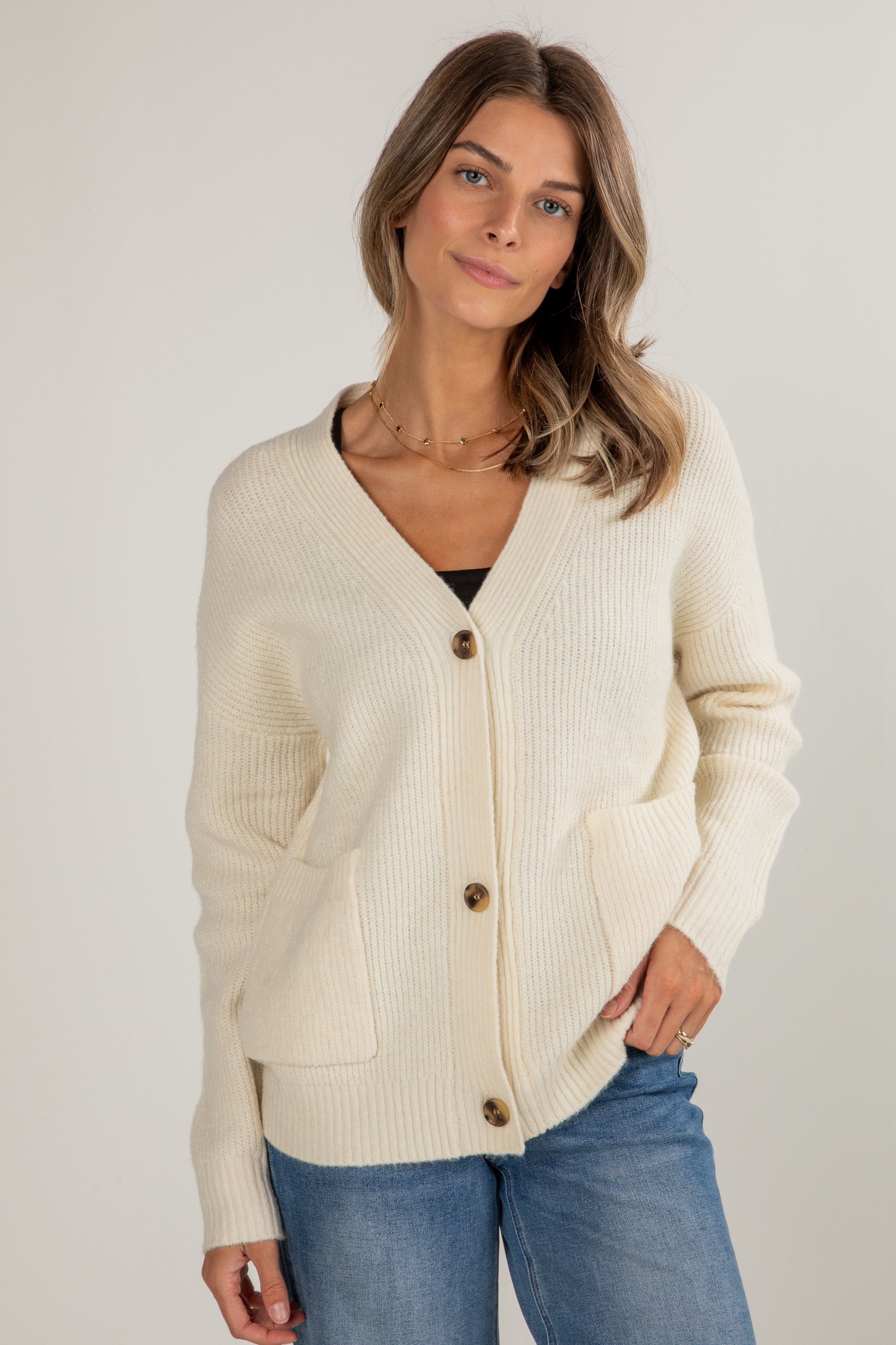 Woman wearing a cream cardigan with buttons on a plain background