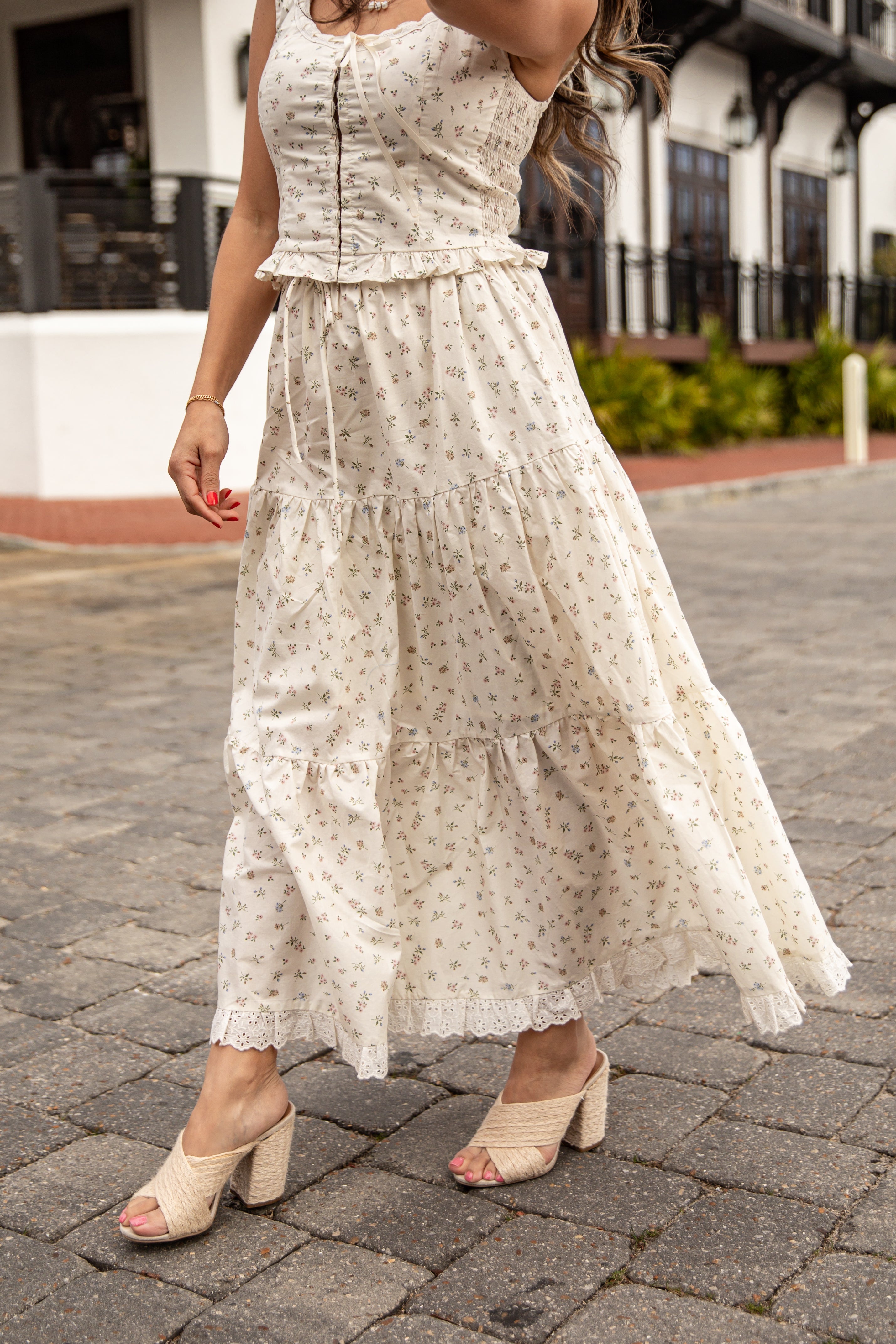 Woman wearing a white floral dress on a paved street.