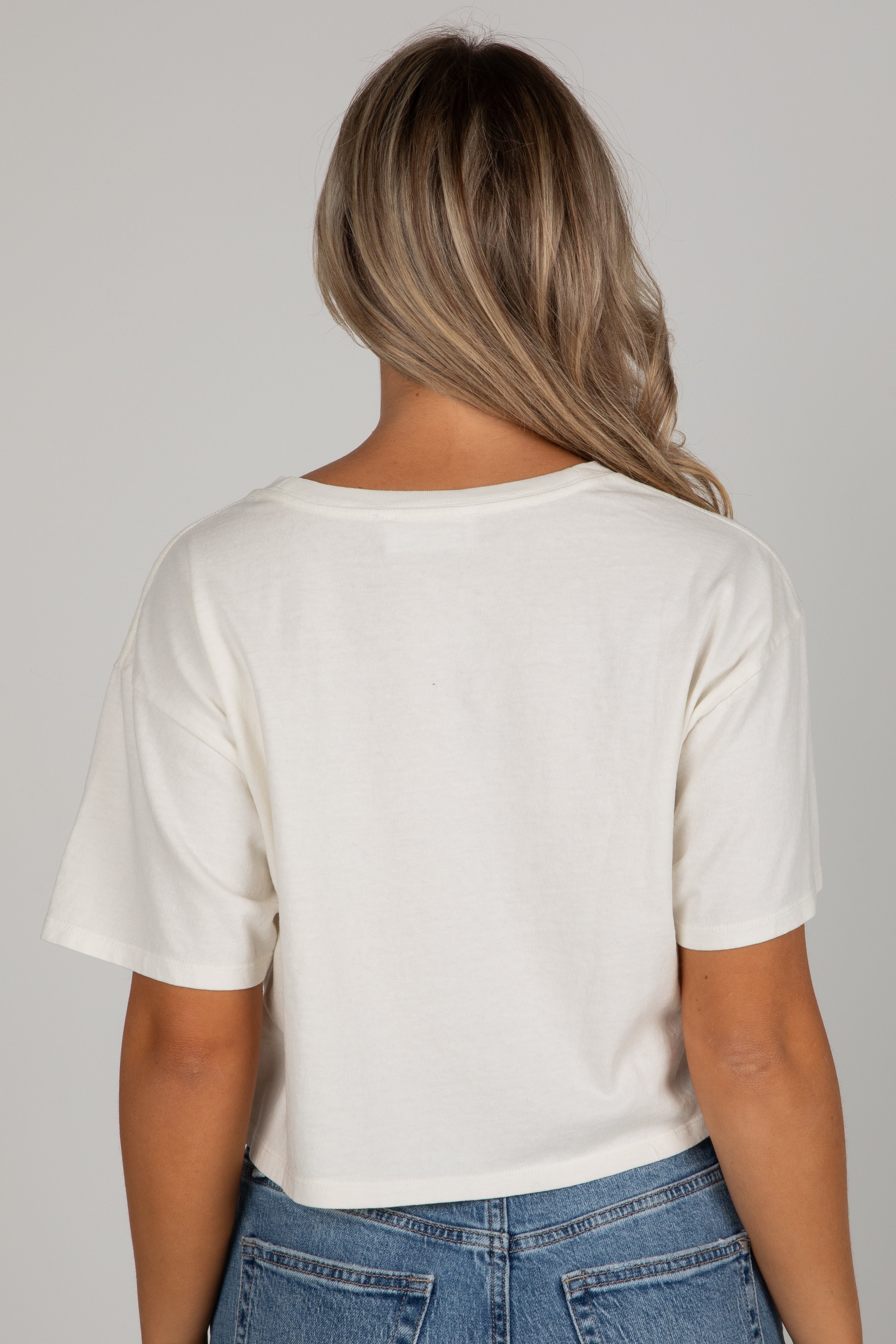 Person wearing a white t-shirt and blue jeans against a gray background